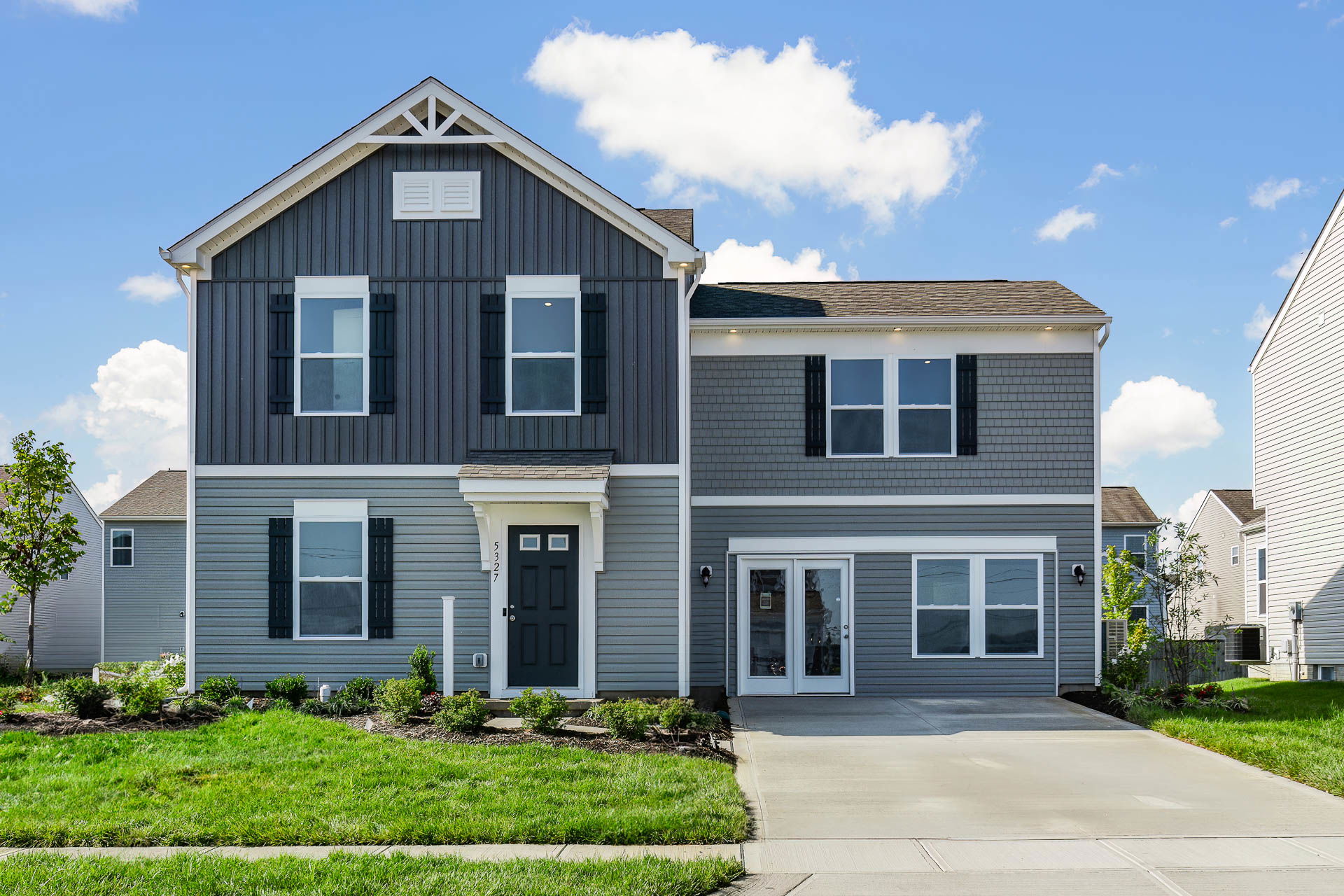 Modern two-story gray house with a neatly landscaped front yard and a wide driveway under a blue sky.