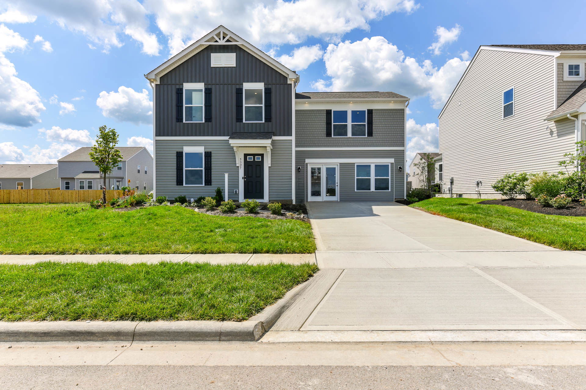 Modern two-story gray house with a manicured lawn and driveway on a sunny day.
