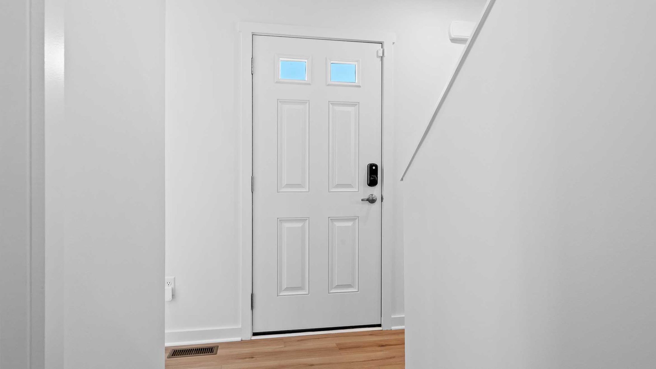 White entryway with a wooden floor featuring a closed front door with a digital lock and two small windows.