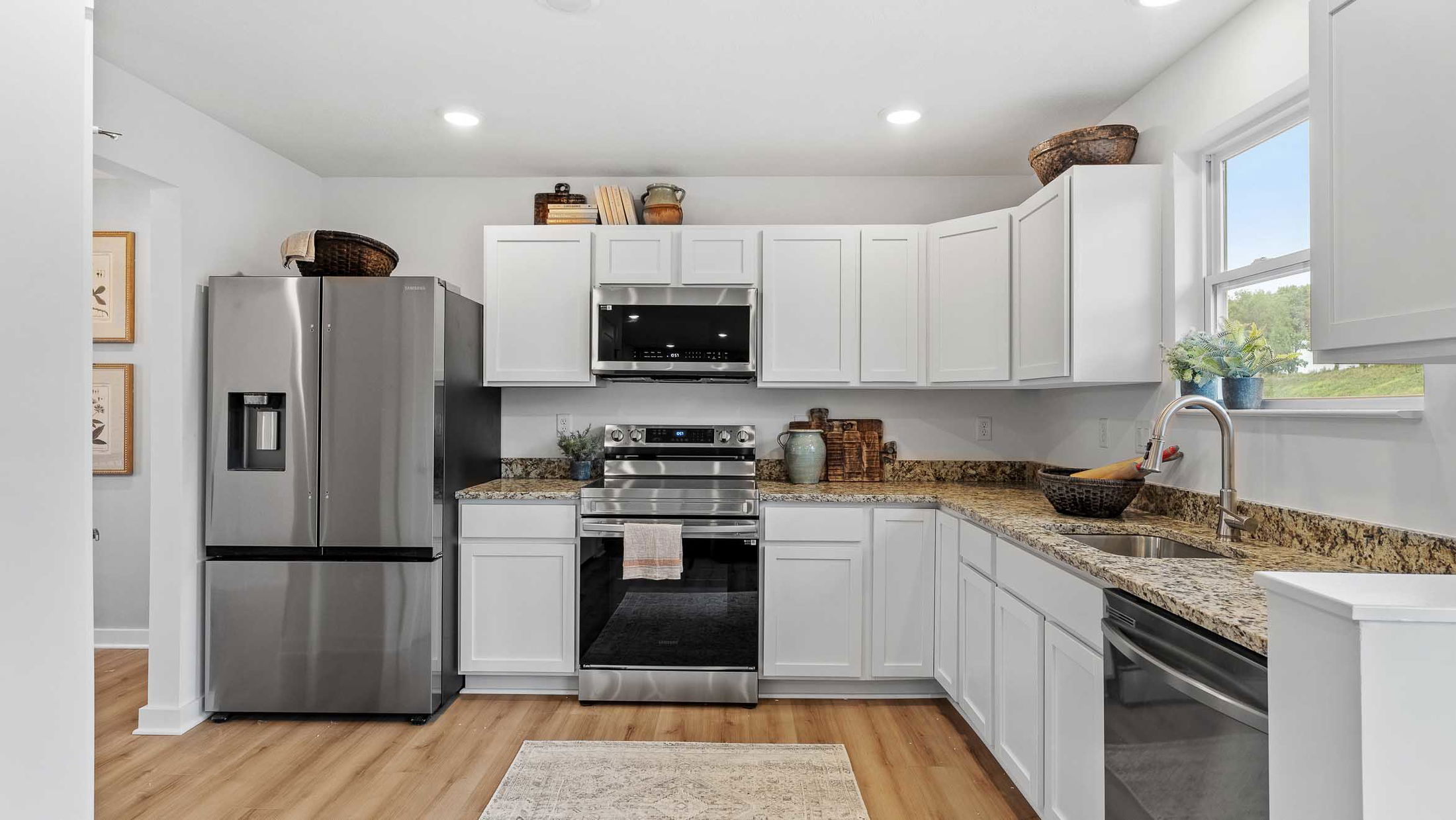 Modern kitchen with stainless steel appliances, white cabinets, granite countertops, and wooden flooring.