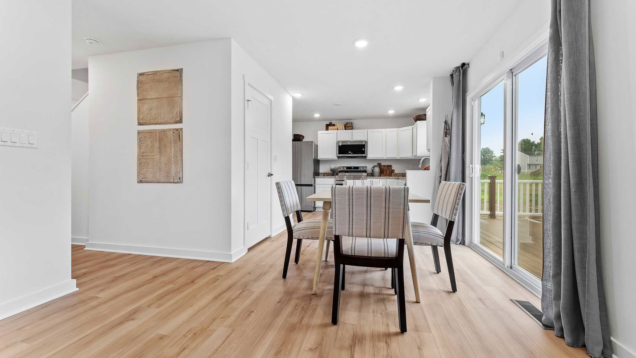 Modern open-concept dining and kitchen area with wooden floors and large sliding glass doors opening to a deck.