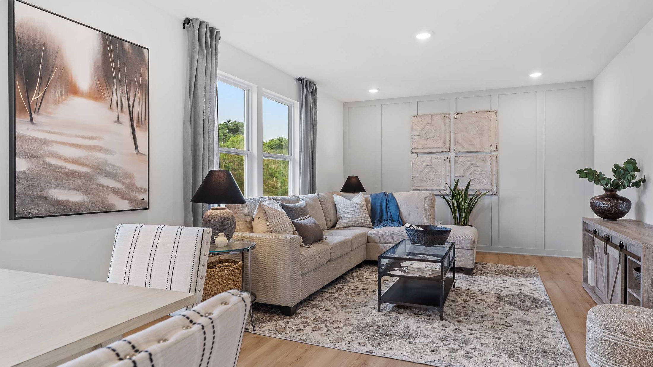 Modern living room with stylish decor, featuring a beige sectional sofa, abstract artwork, and a patterned area rug.