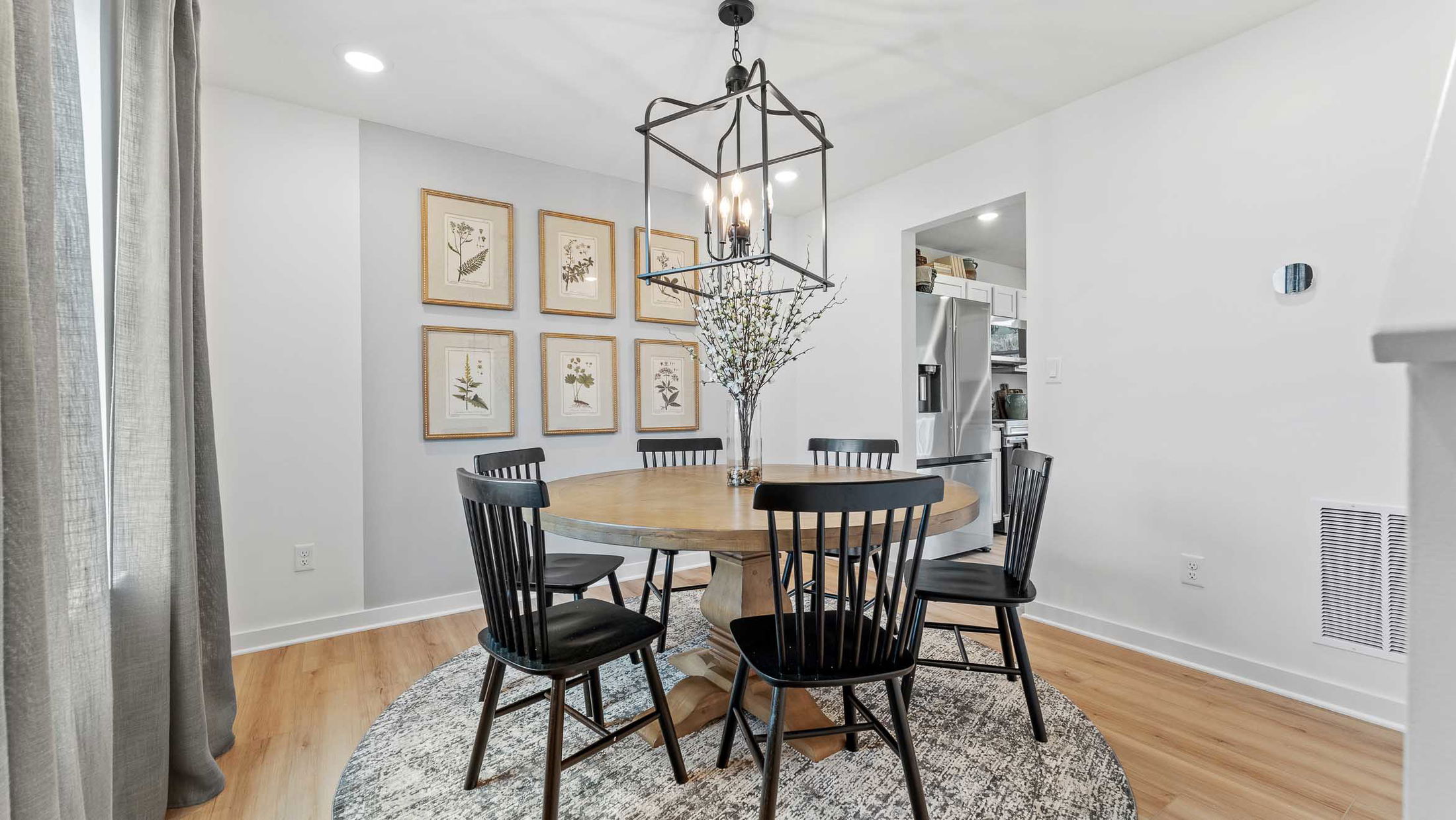 Stylish dining room with a round wooden table, black chairs, a modern chandelier, and botanical wall art.