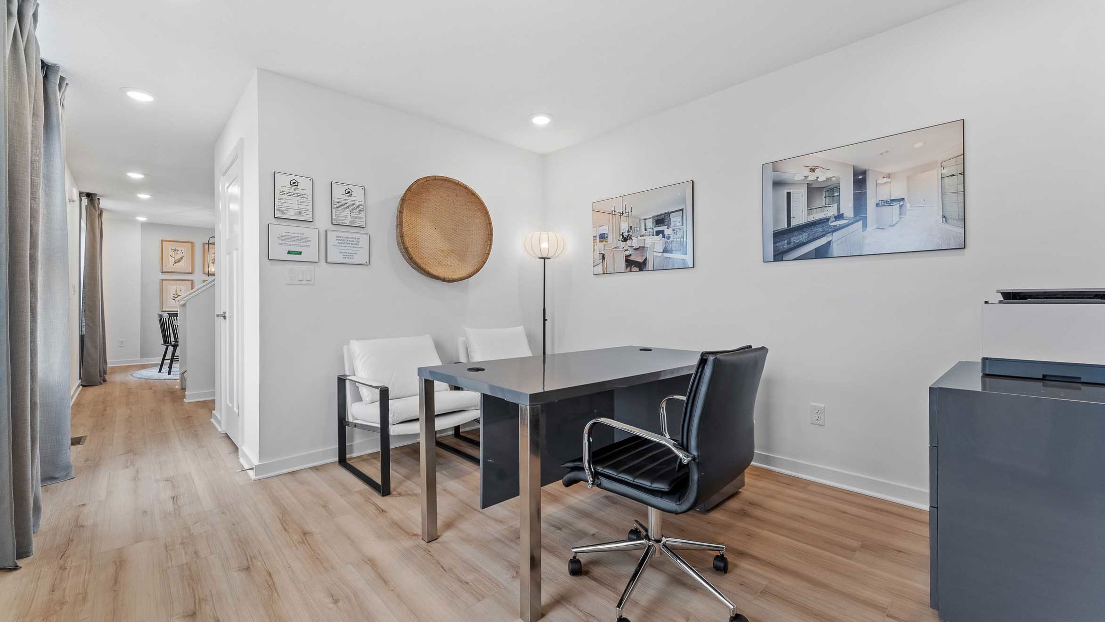 Modern office interior with sleek black desk, white chairs, and framed wall art in a bright, minimalist setting.