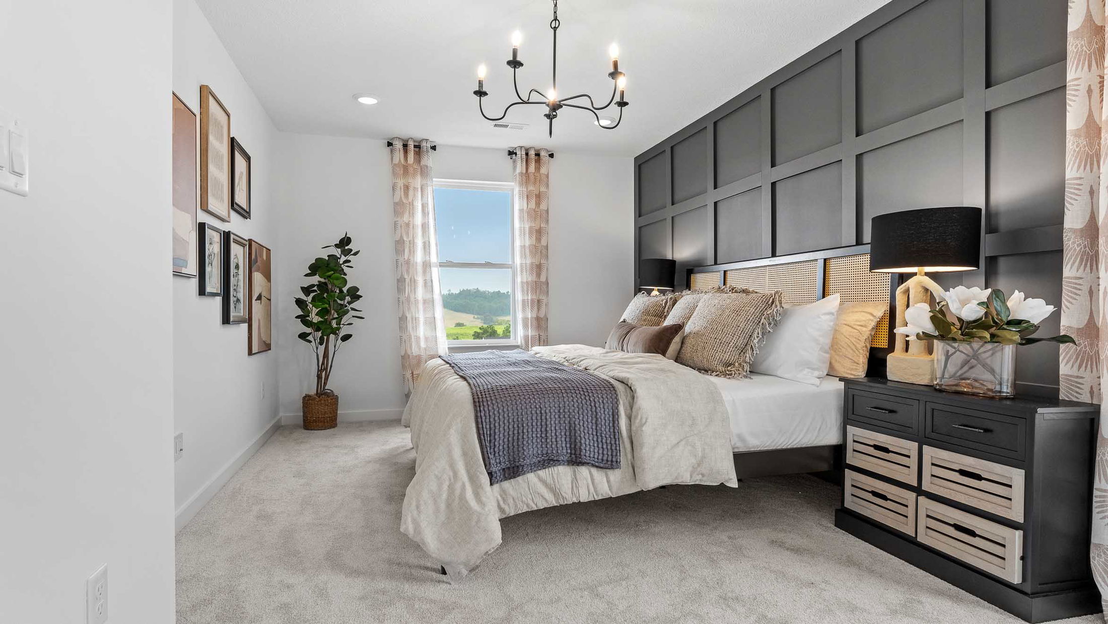Modern bedroom with elegant decor, featuring a stylish bed, dark accent wall, framed artwork, and a large window with scenic views.