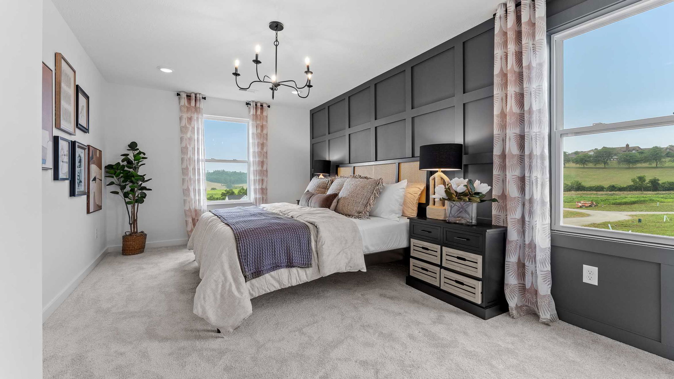 Stylish modern bedroom with gray accent wall, elegant chandelier, and scenic countryside views through large windows.