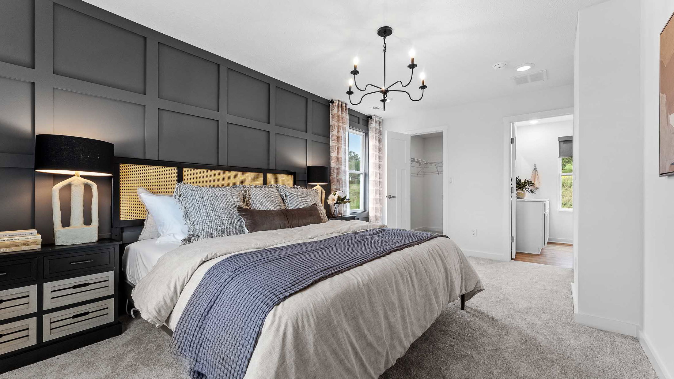 Stylish modern bedroom with black paneled accent wall, cozy bedding, and contemporary chandelier lighting.