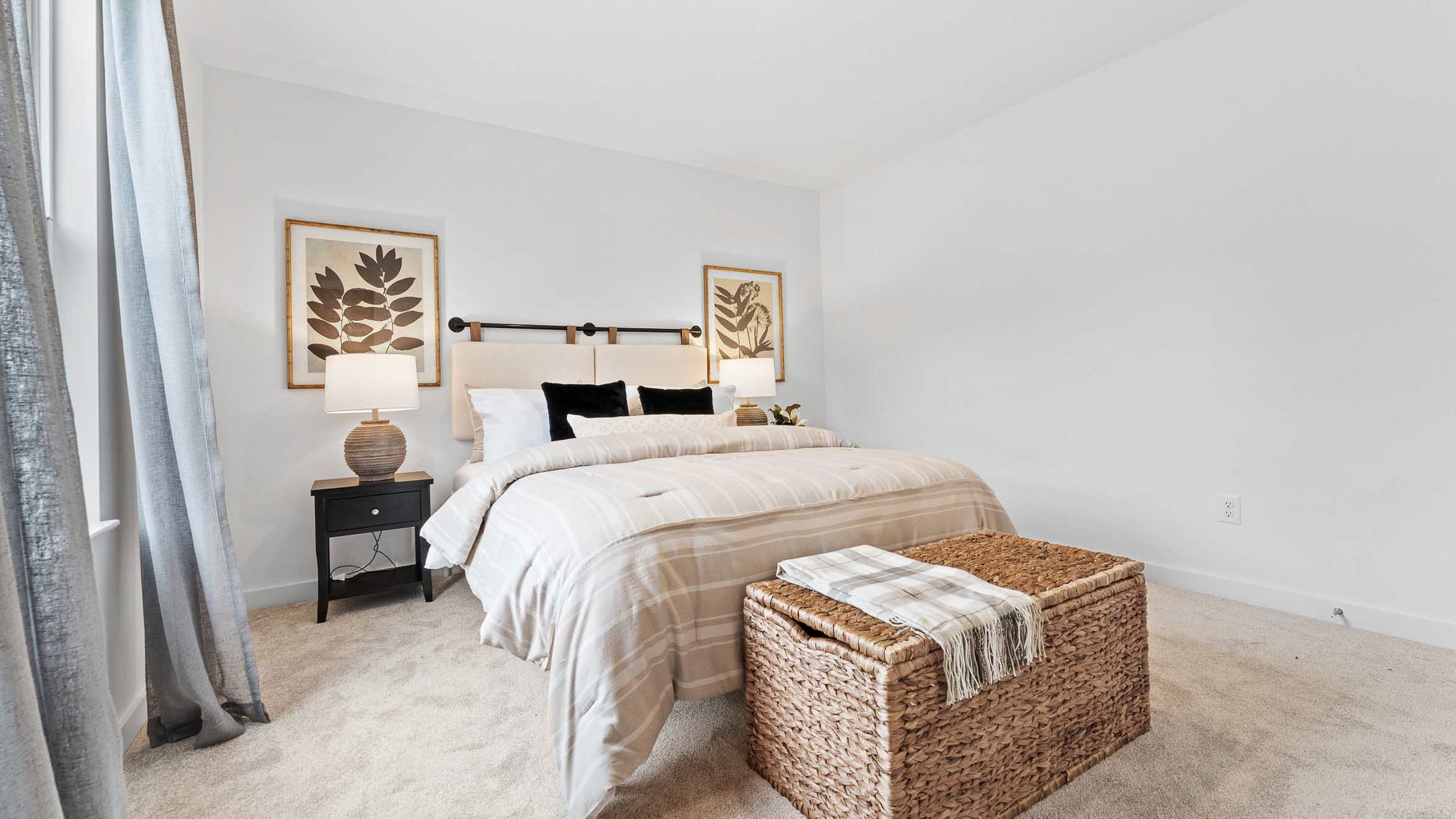Cozy bedroom featuring a neatly made bed with striped bedding, wicker storage bench, and elegant decor with framed leaf artwork above.