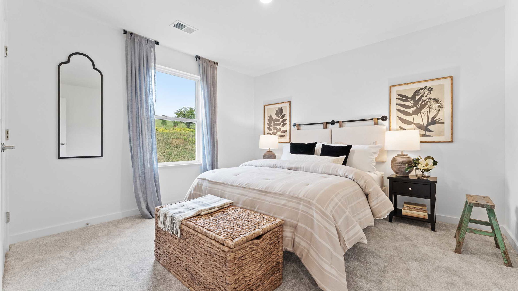 Modern bedroom with neutral tones, featuring a cozy bed, woven storage bench, and stylish decor elements.