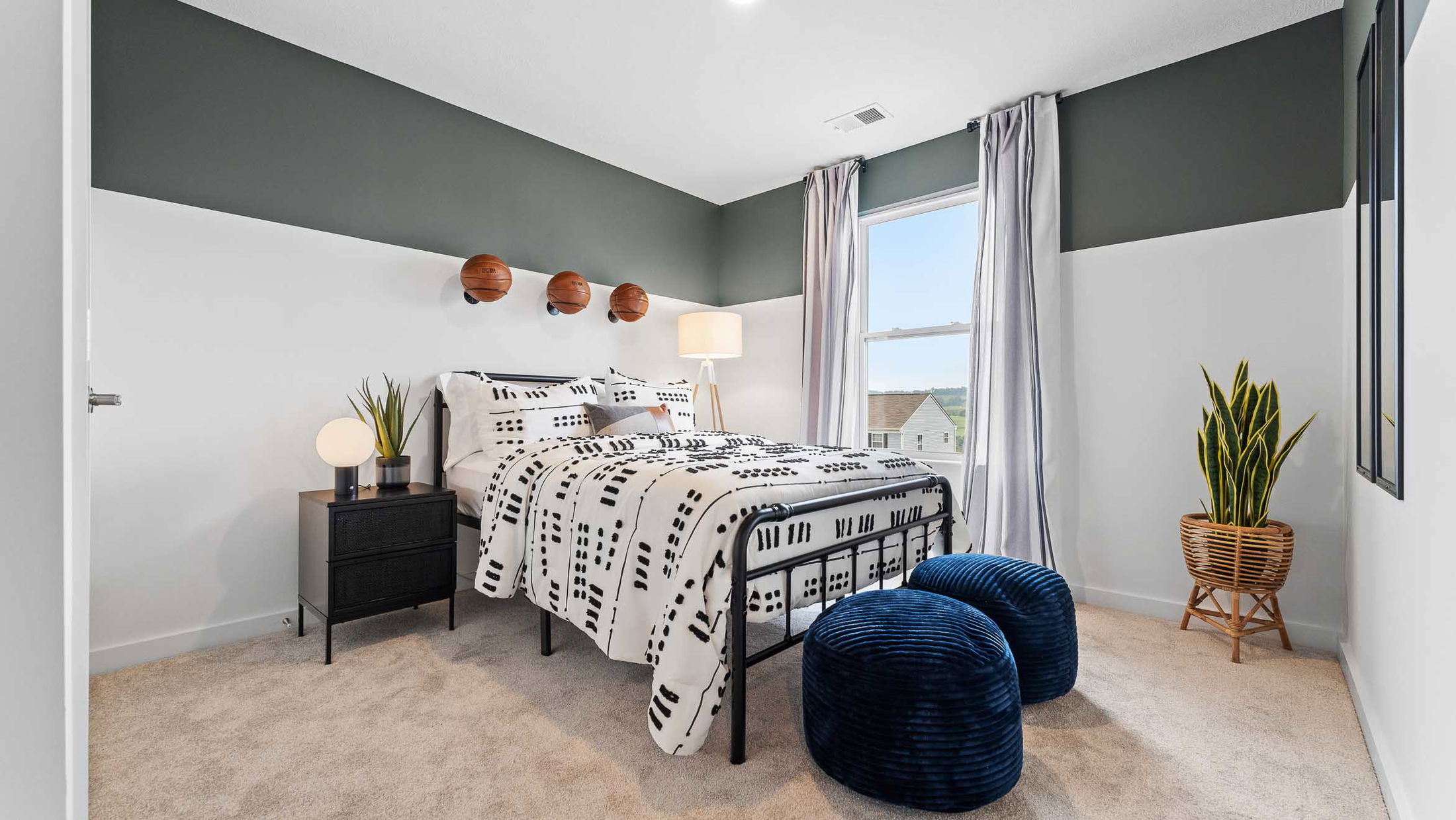 Modern bedroom with monochrome bedding, basketball wall decor, and large windows featuring greenery and stylish accents.