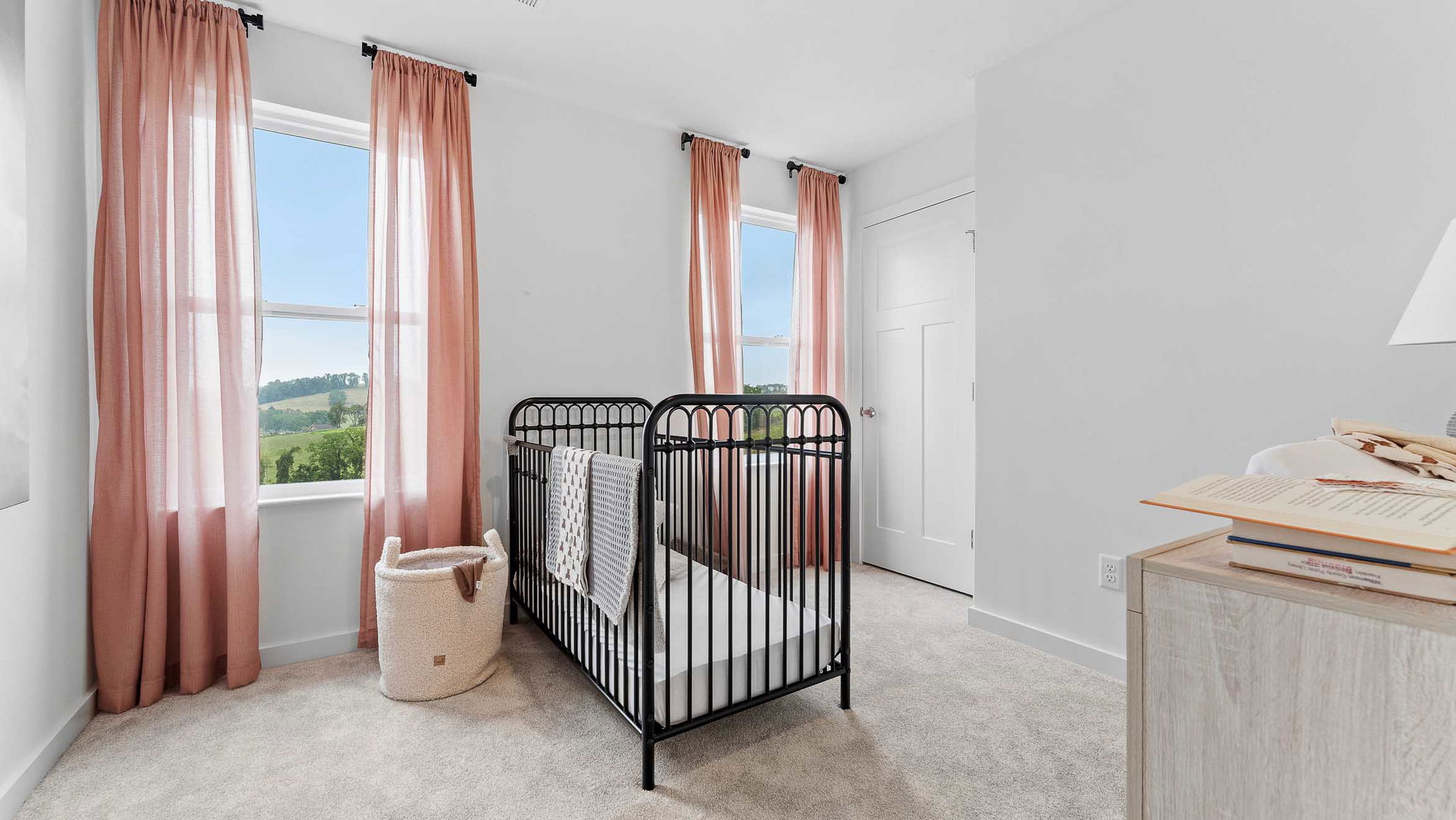 Modern nursery room with a black metal crib, soft pink curtains, and a cozy, neutral decor.