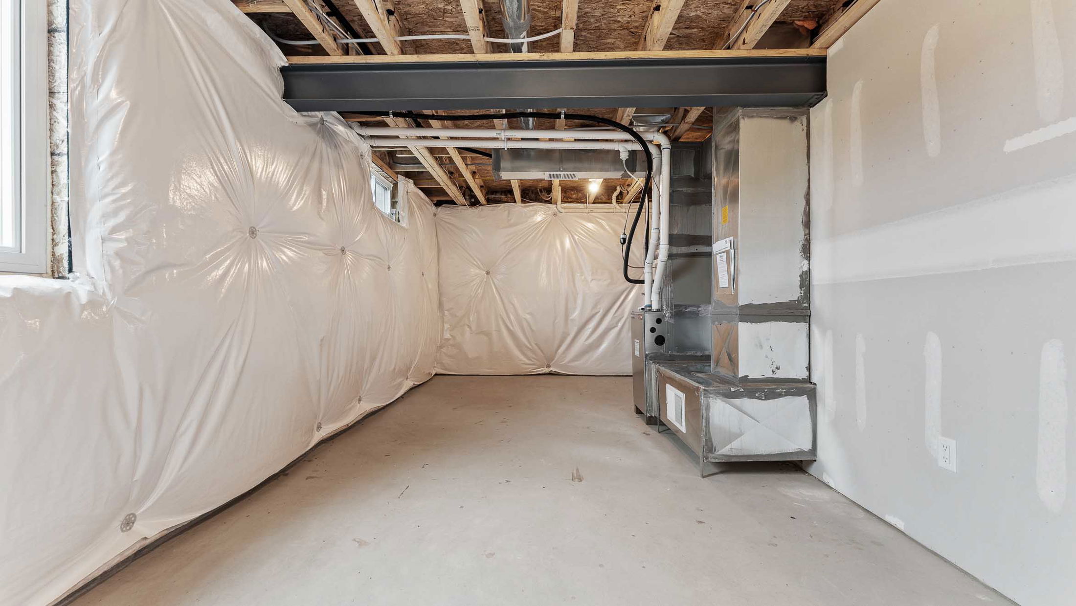 Unfinished basement with exposed ceiling beams, insulation on walls, and an HVAC system.