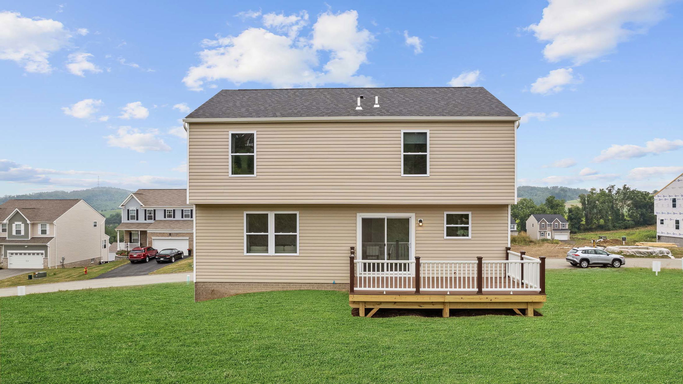 Modern two-story suburban home with a backyard deck, surrounded by other houses and scenic hills under a blue sky.