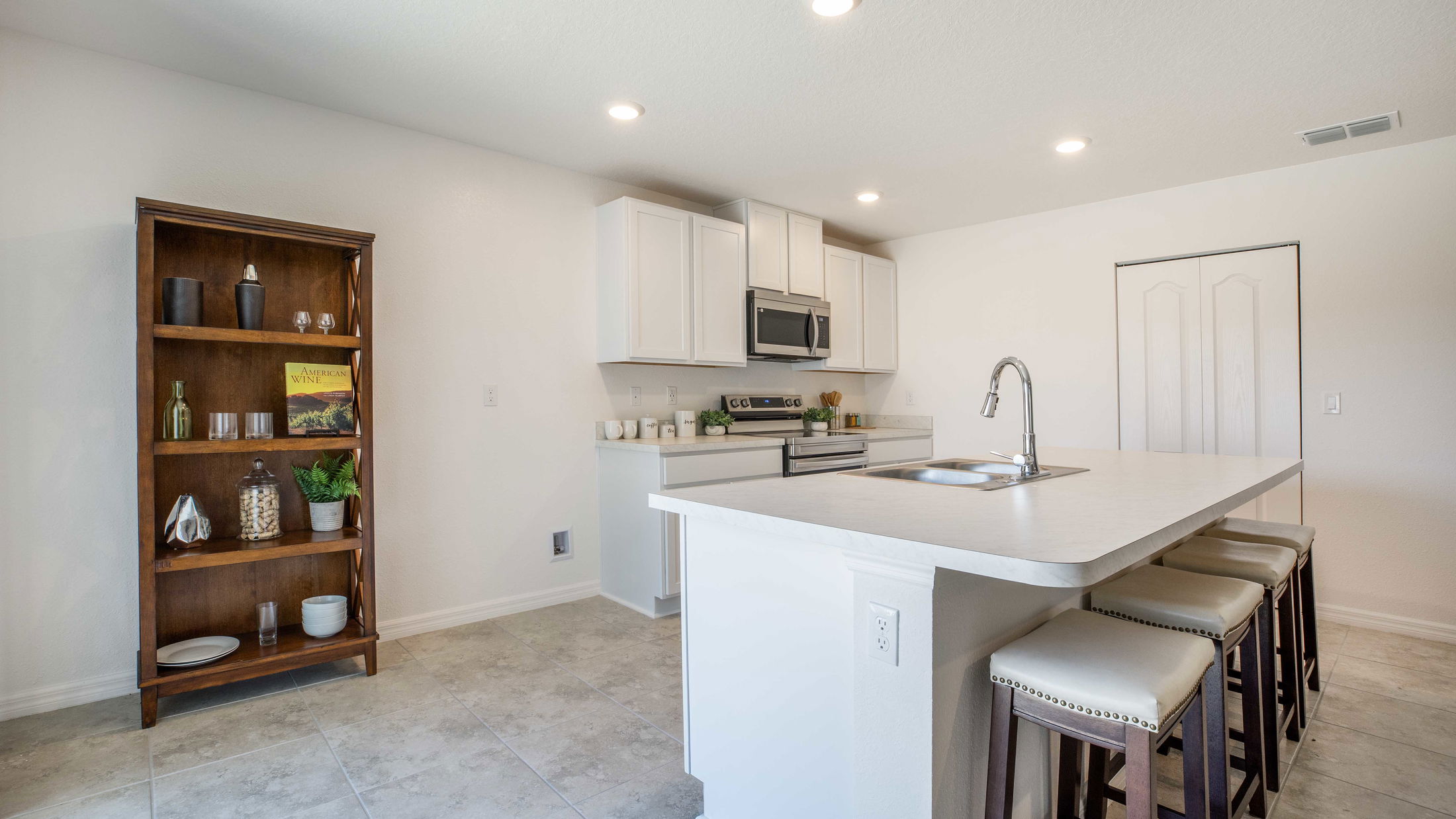 Modern kitchen with white cabinetry, stainless steel appliances, a spacious island with bar stools, and a decorative shelving unit.