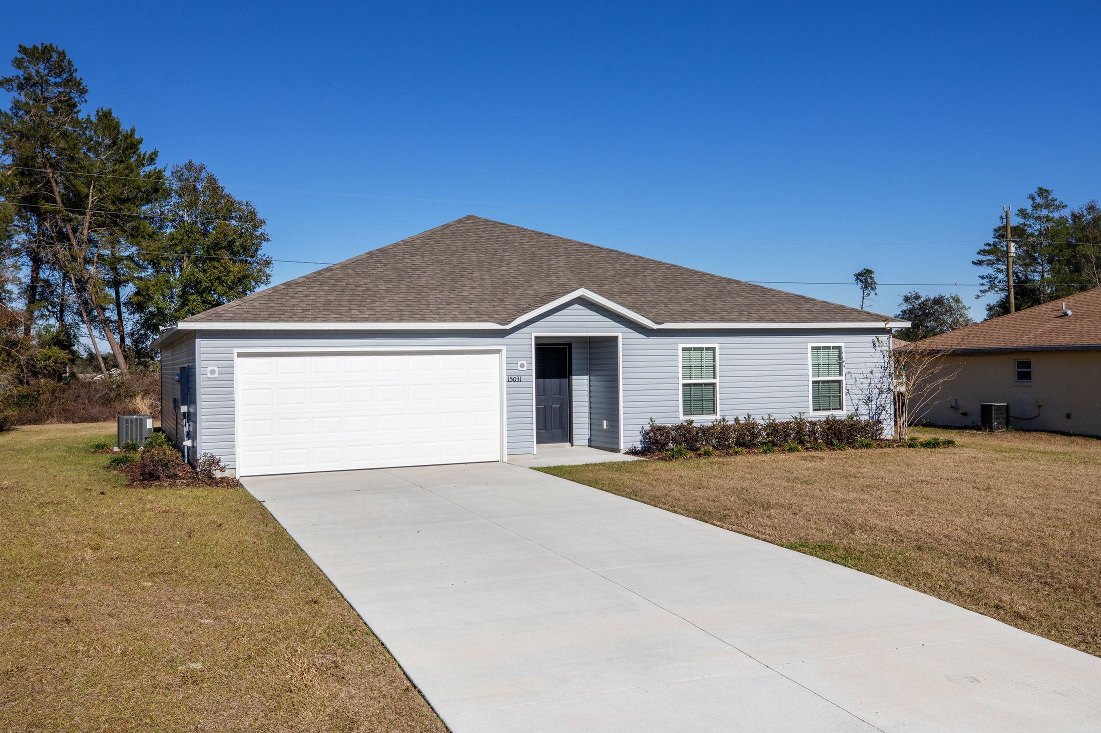 Single-story, gray suburban house with a two-car garage, driveway, and lawn on a clear day.