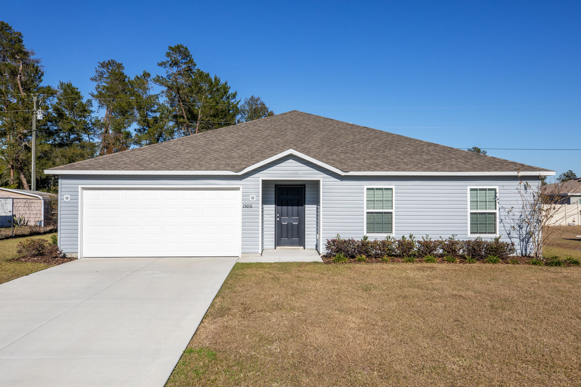 Single-story suburban home with gray siding, a two-car garage, and well-maintained front yard under clear blue sky.