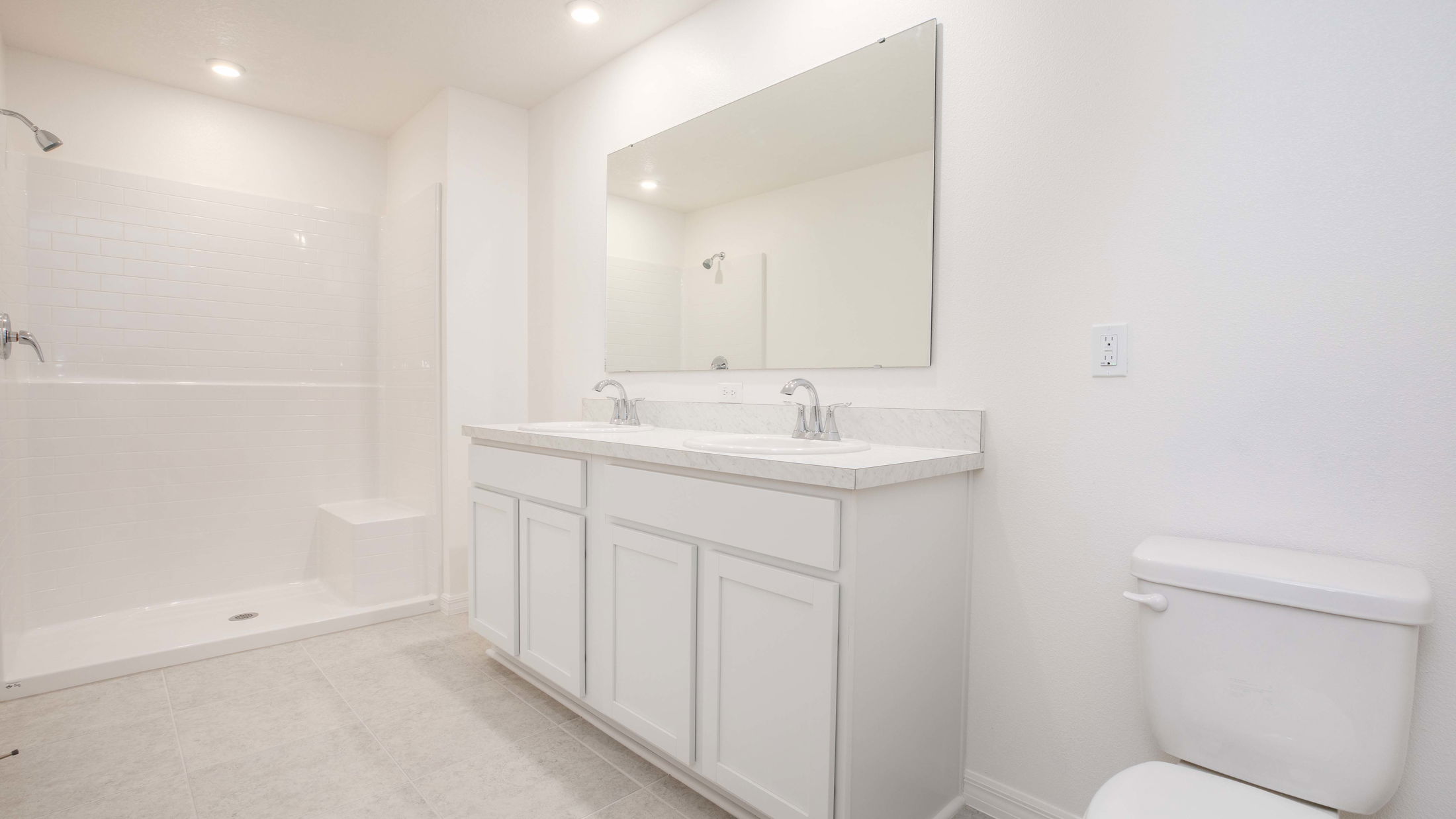 Bright, modern bathroom with a large mirror, double vanity, spacious shower, and white tile flooring.
