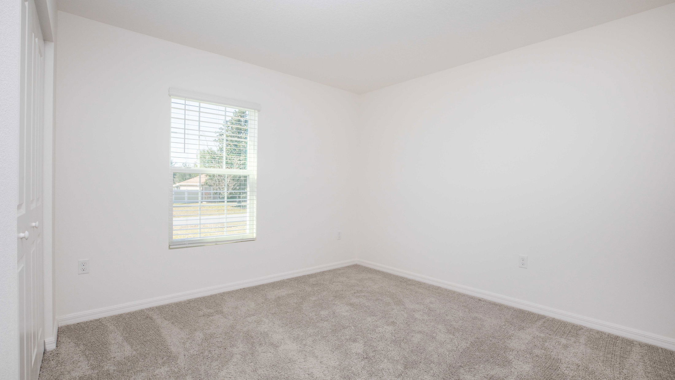 Empty room with white walls, carpeted floor, and a window with blinds.