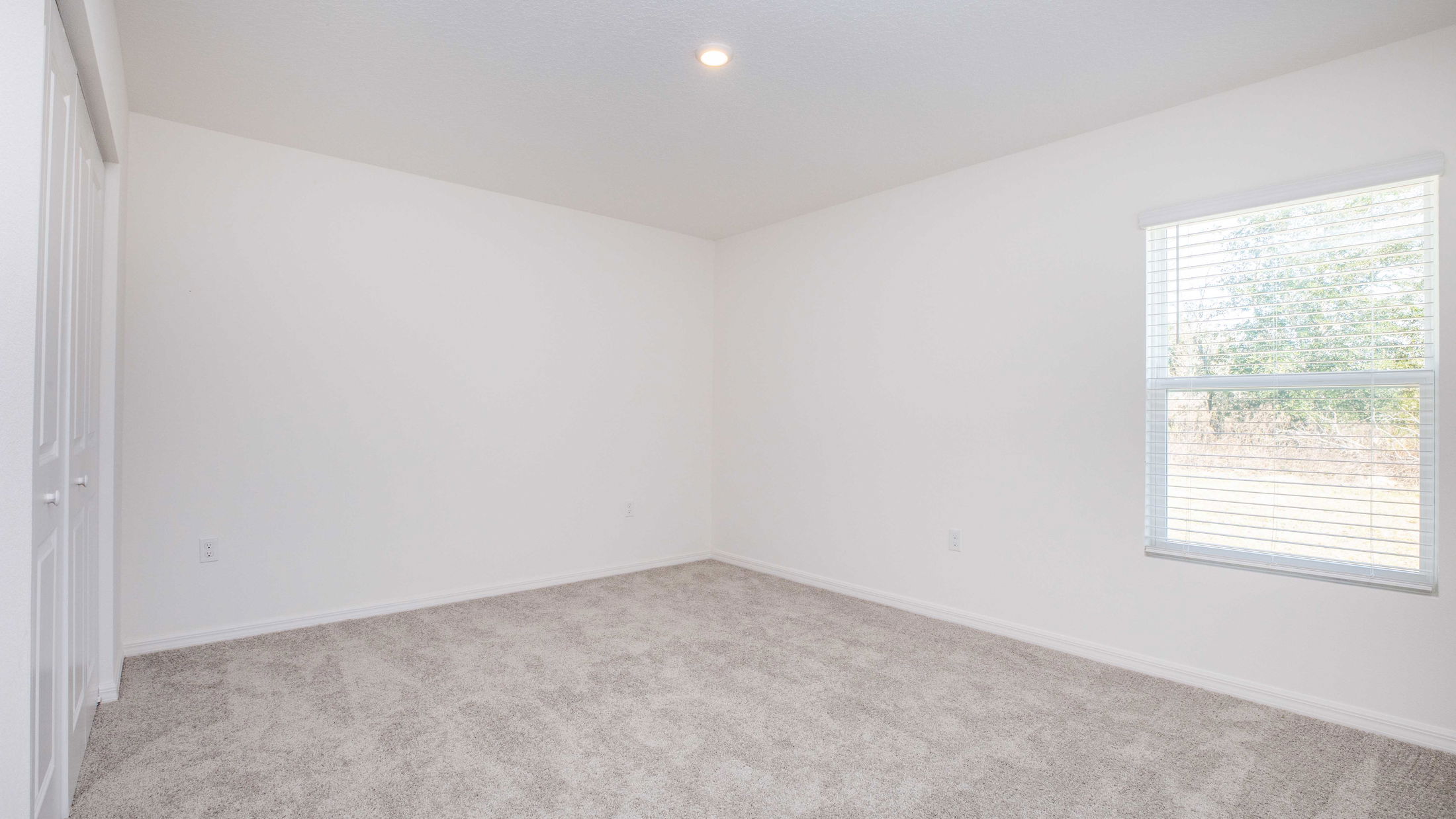 Empty room with white walls, beige carpet, recessed ceiling light, and a window with blinds.