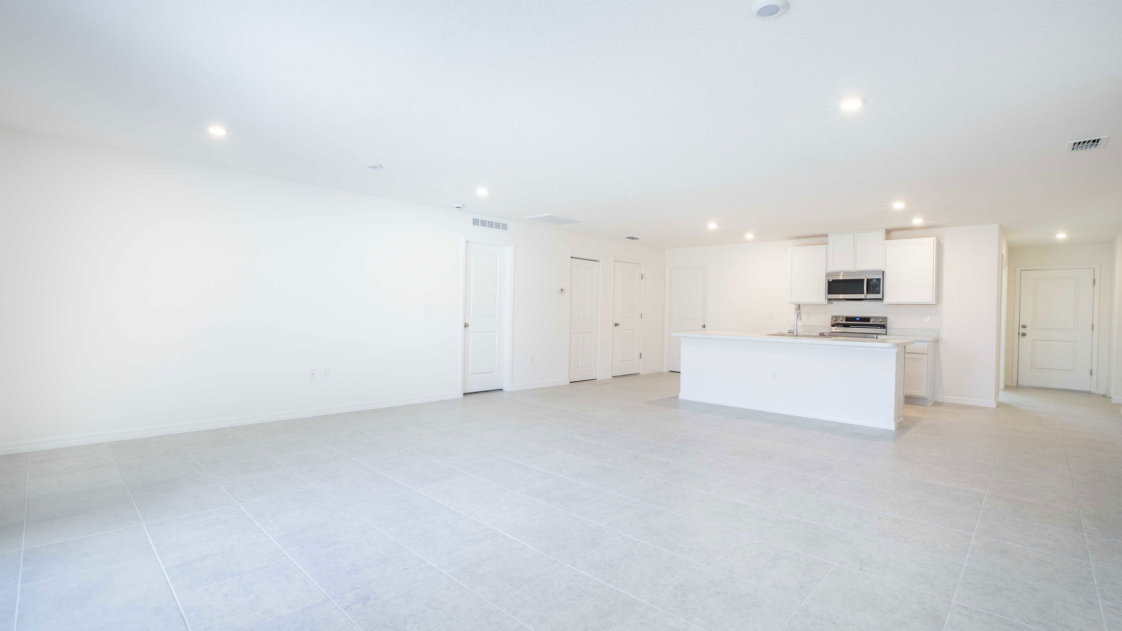 Bright, modern open-concept kitchen and living area with white walls and tile flooring.