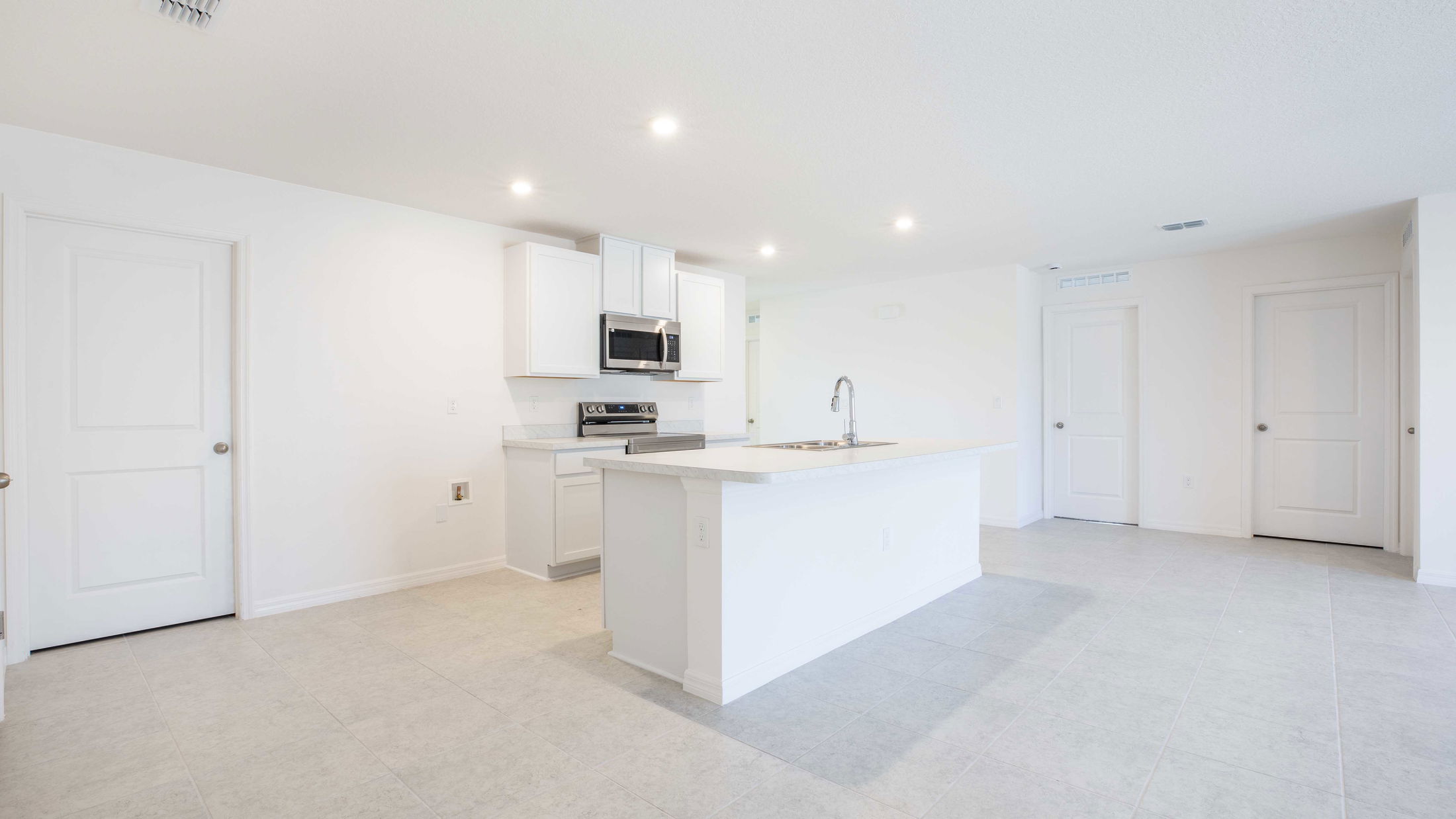 Modern, bright kitchen with white cabinets, island, stainless steel appliances, and tile flooring in a spacious open-concept layout.
