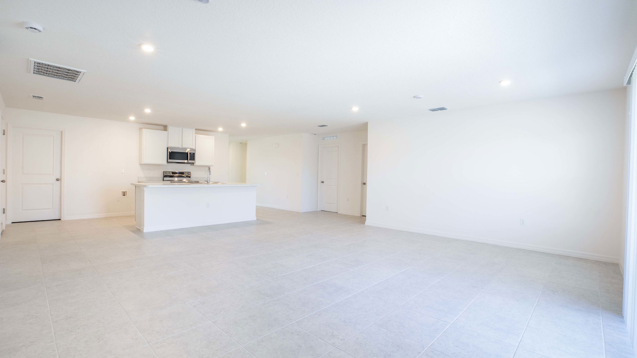 Modern, spacious open-concept kitchen and living area with light gray tile flooring and white walls.