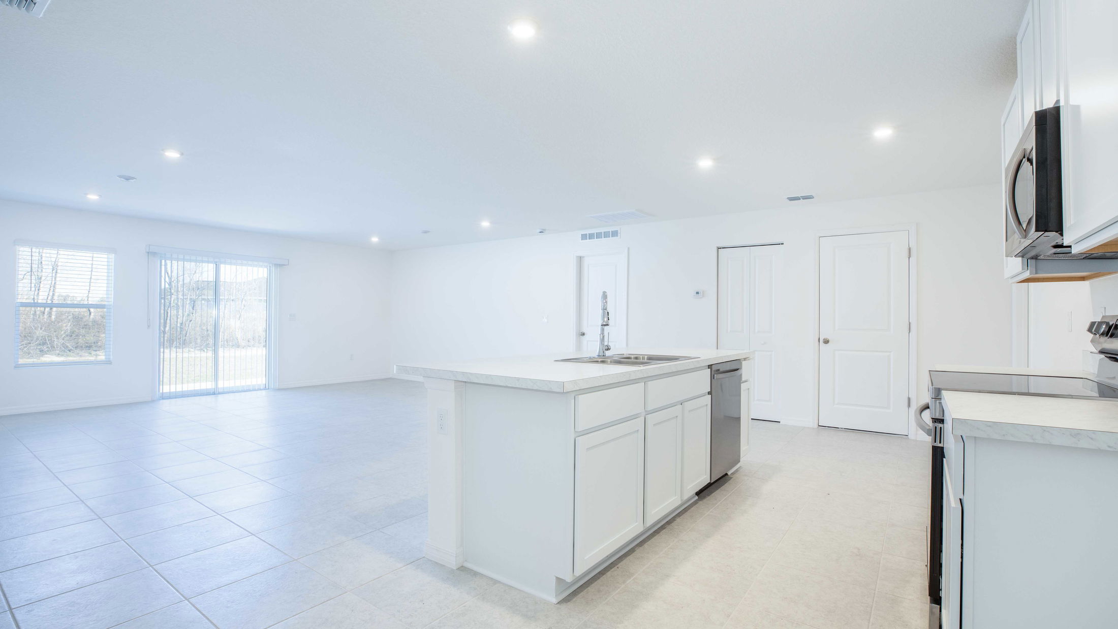 Modern open-concept kitchen with white cabinetry, a central island, and large tile flooring in a bright, spacious room.