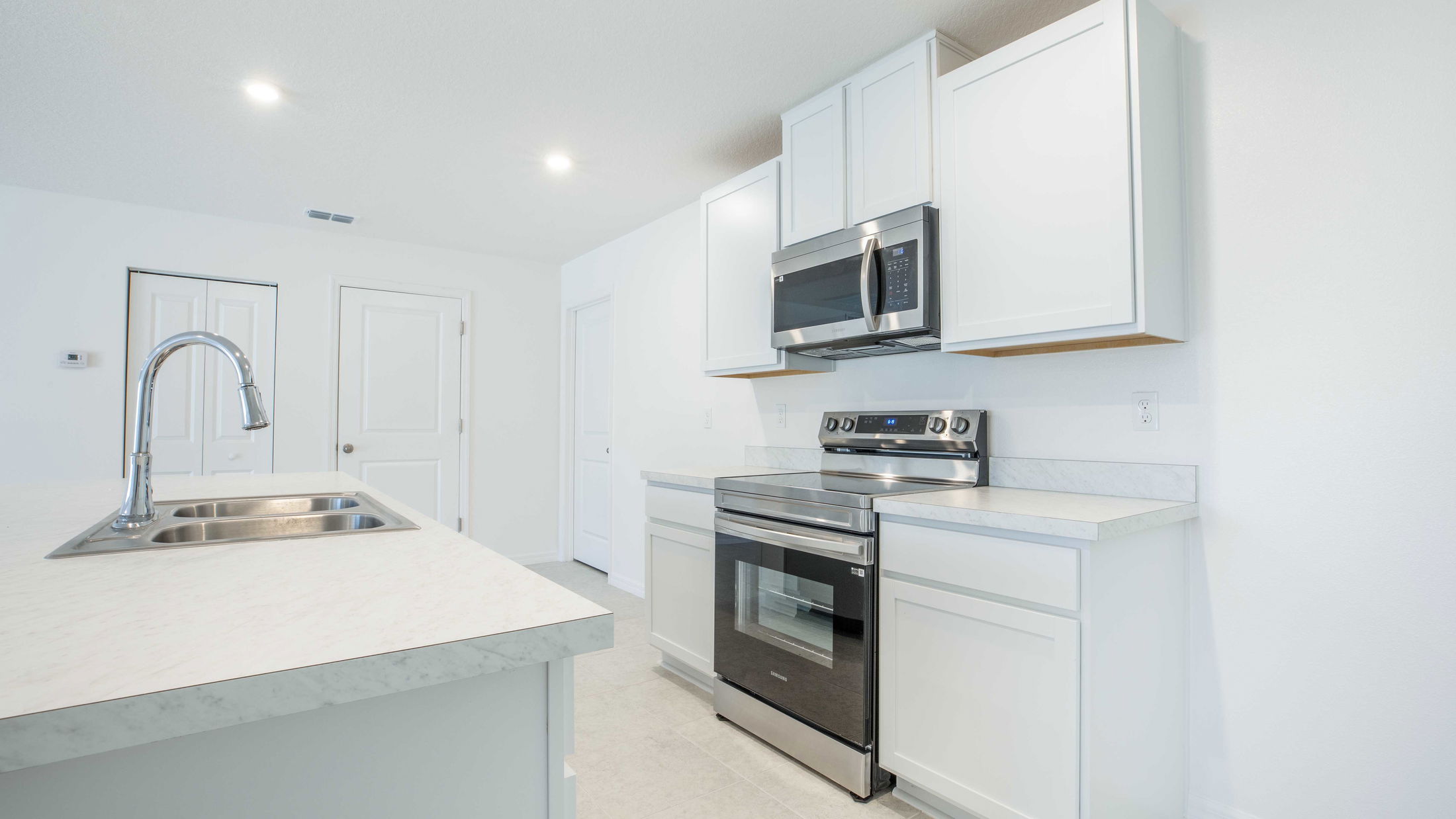 Modern kitchen with stainless steel appliances, white cabinets, and a sleek marble countertop with a double sink.