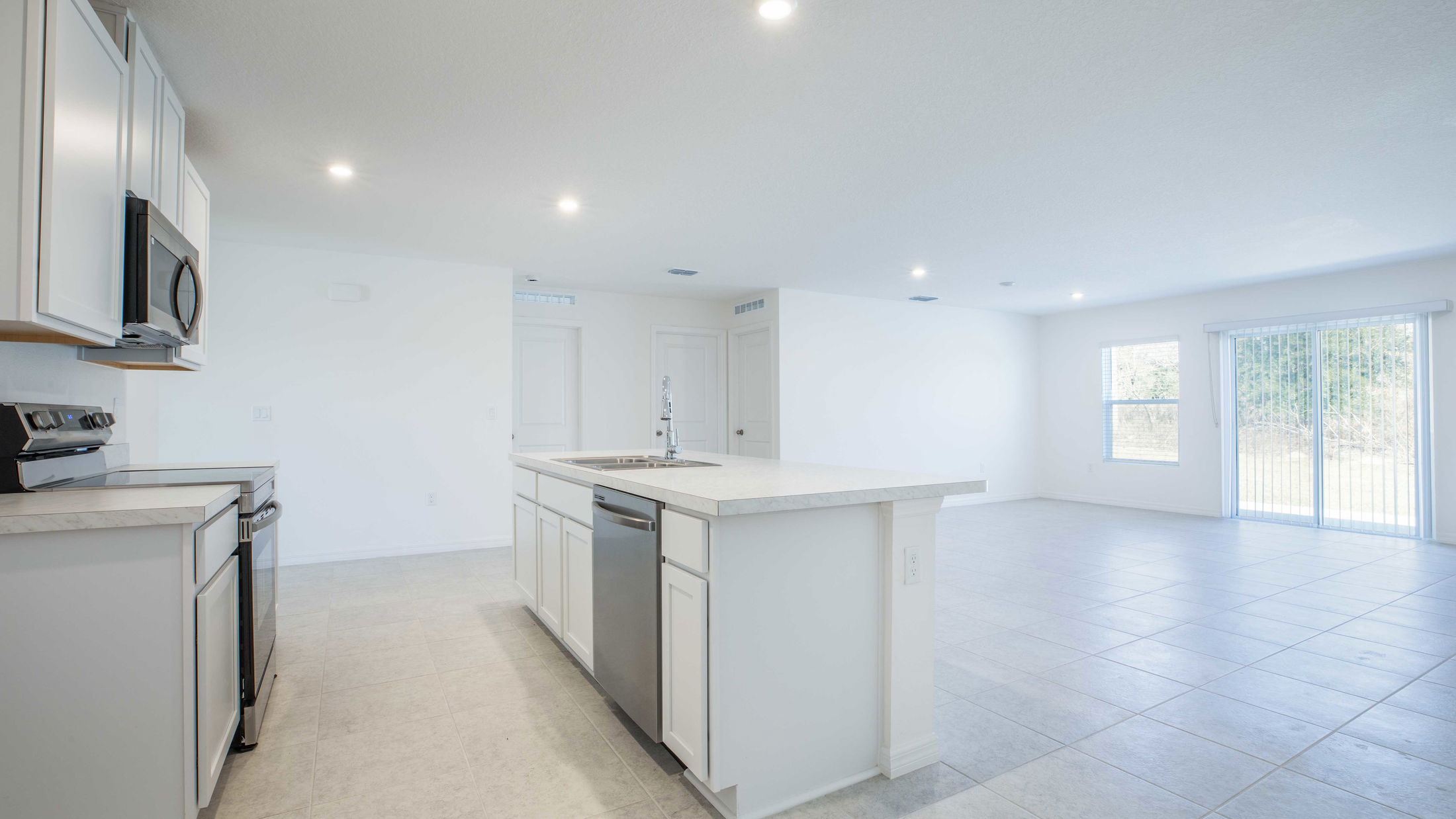 Modern kitchen with white cabinets, stainless steel appliances, large island, and an open-concept layout leading to a bright living area.