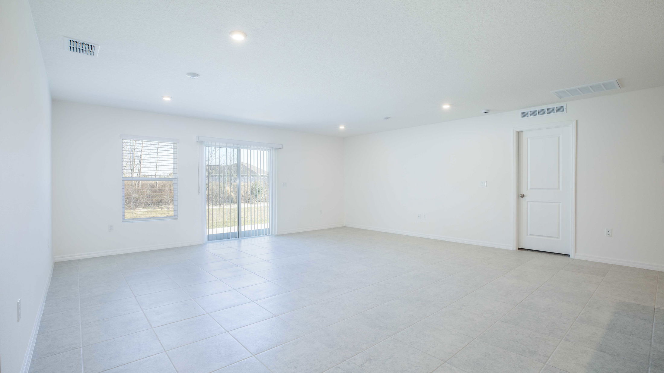 Spacious empty room with light gray tile flooring, white walls, and large windows providing natural light.