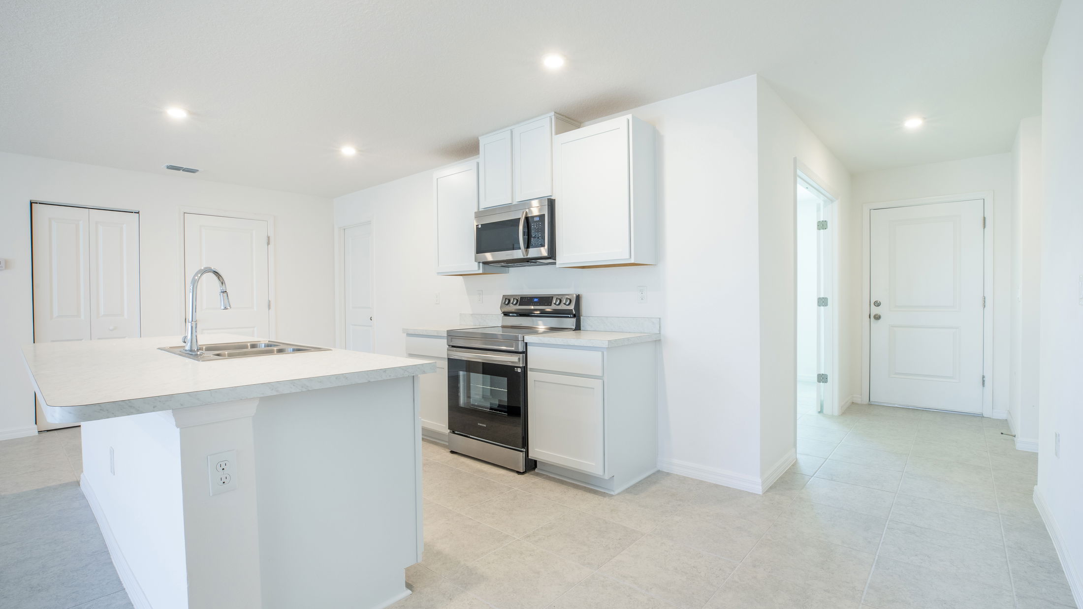Modern kitchen interior with white cabinets, stainless steel appliances, and a central island with a sink.