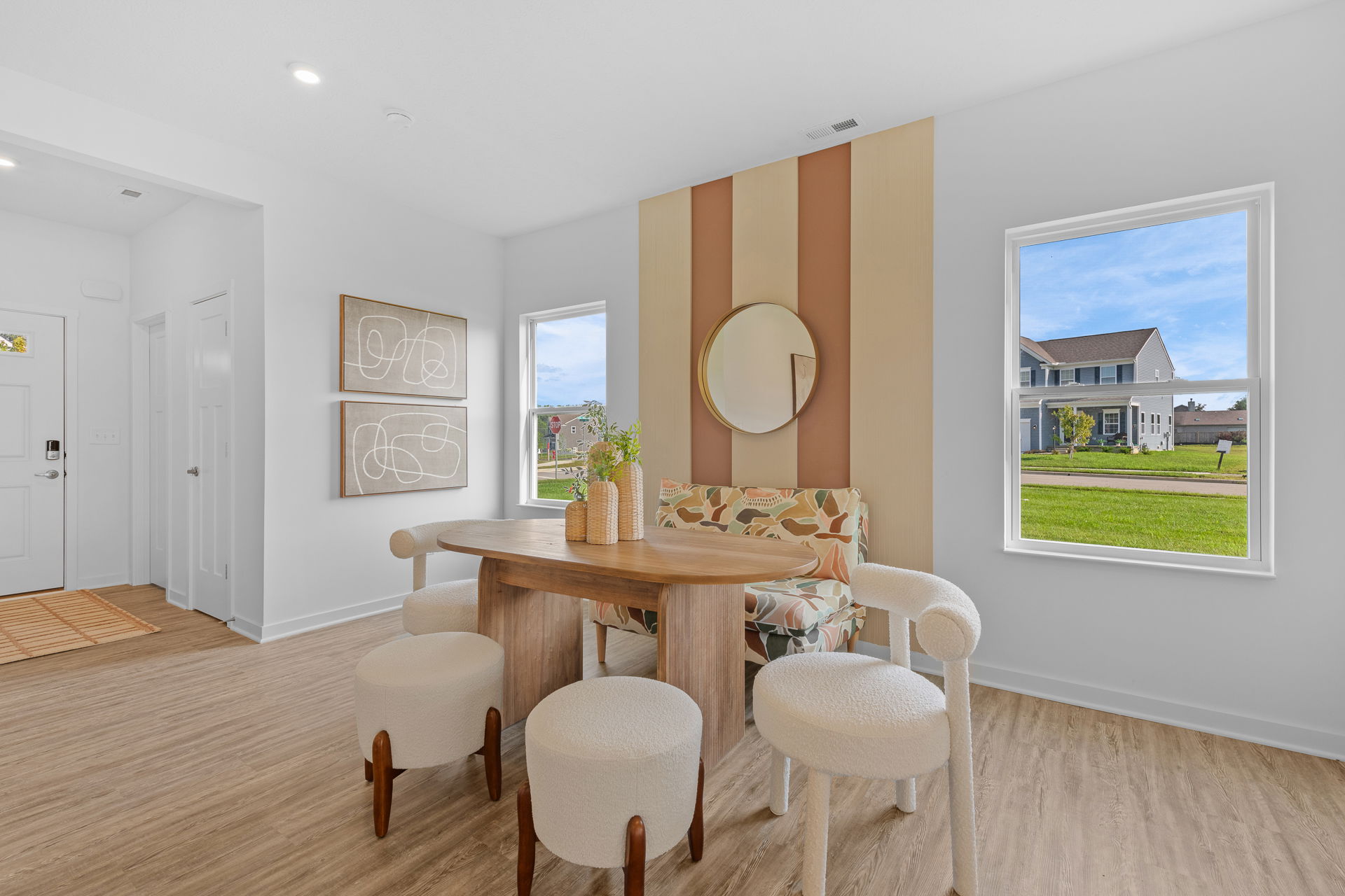 Modern dining area with a wooden table, eclectic chairs, and abstract wall decor, featuring large windows overlooking a suburban neighborhood.