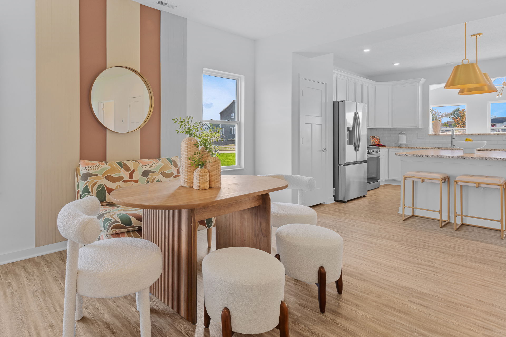 Modern open-plan kitchen and dining area featuring a wooden table, white cushioned seats, and stylish kitchen appliances against a light wood floor.