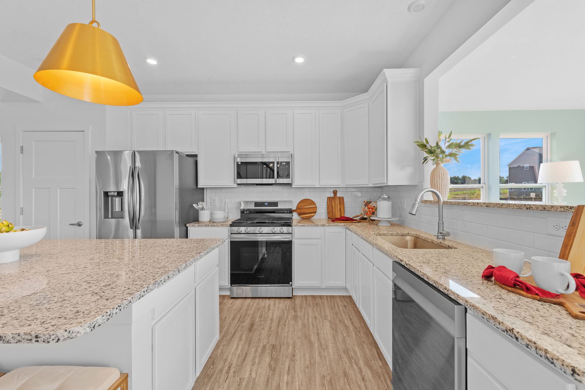 Modern kitchen with white cabinets, stainless steel appliances, and a granite countertop under gold pendant lighting.