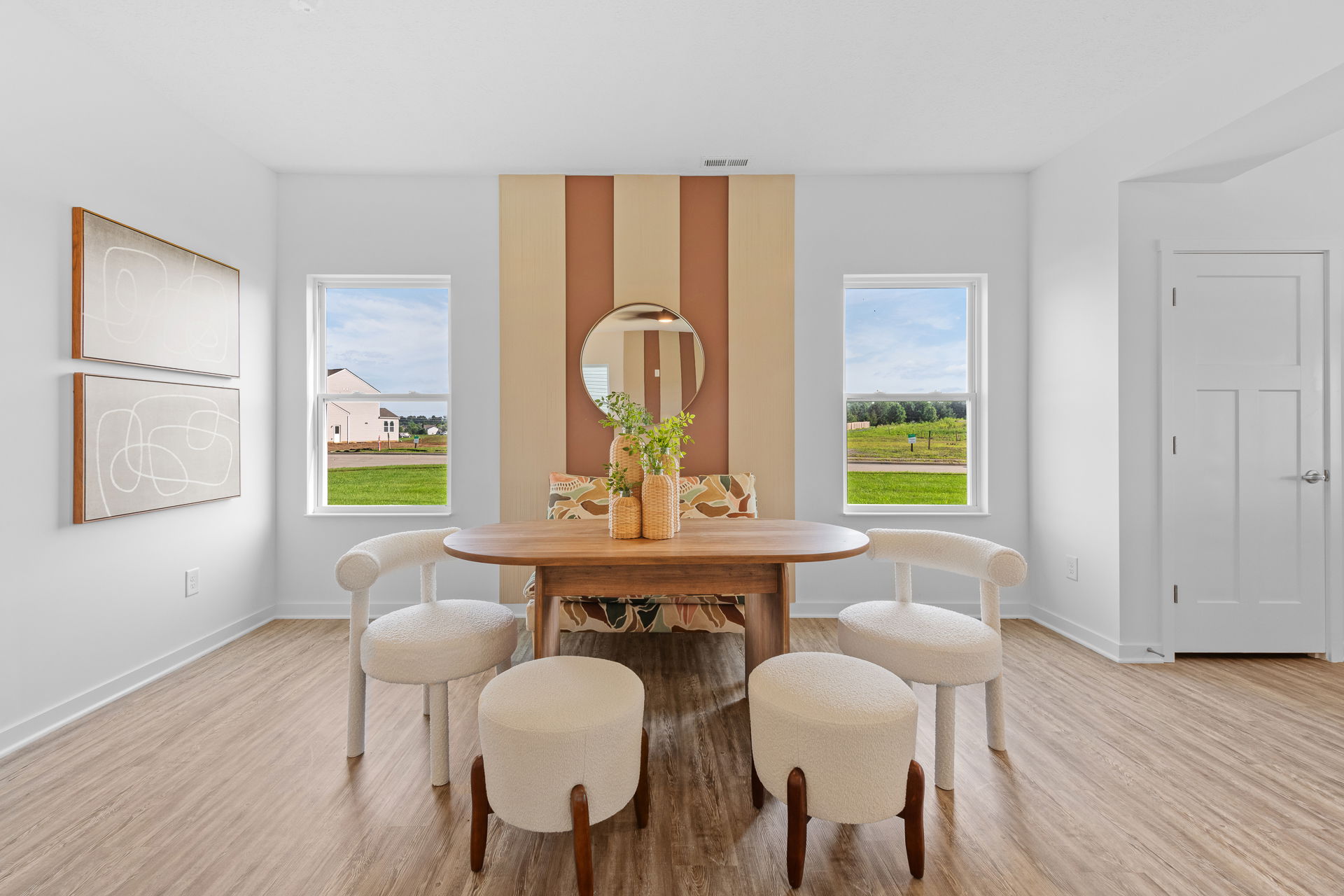 Modern dining room with a wooden table, white chairs, and decorative plants, featuring large windows with scenic views.