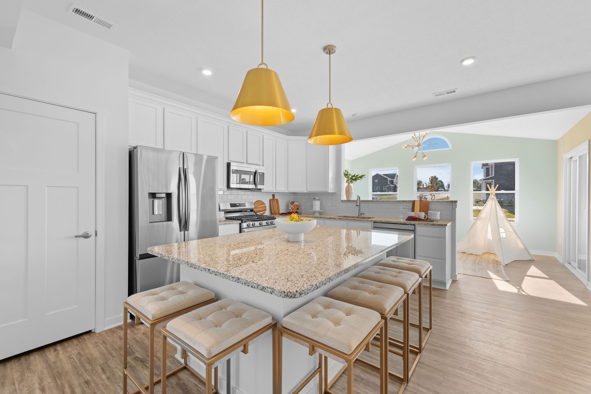 Modern kitchen with a granite island, white cabinets, stainless steel appliances, and golden pendant lights, adjacent to a bright playroom with a small teepee.
