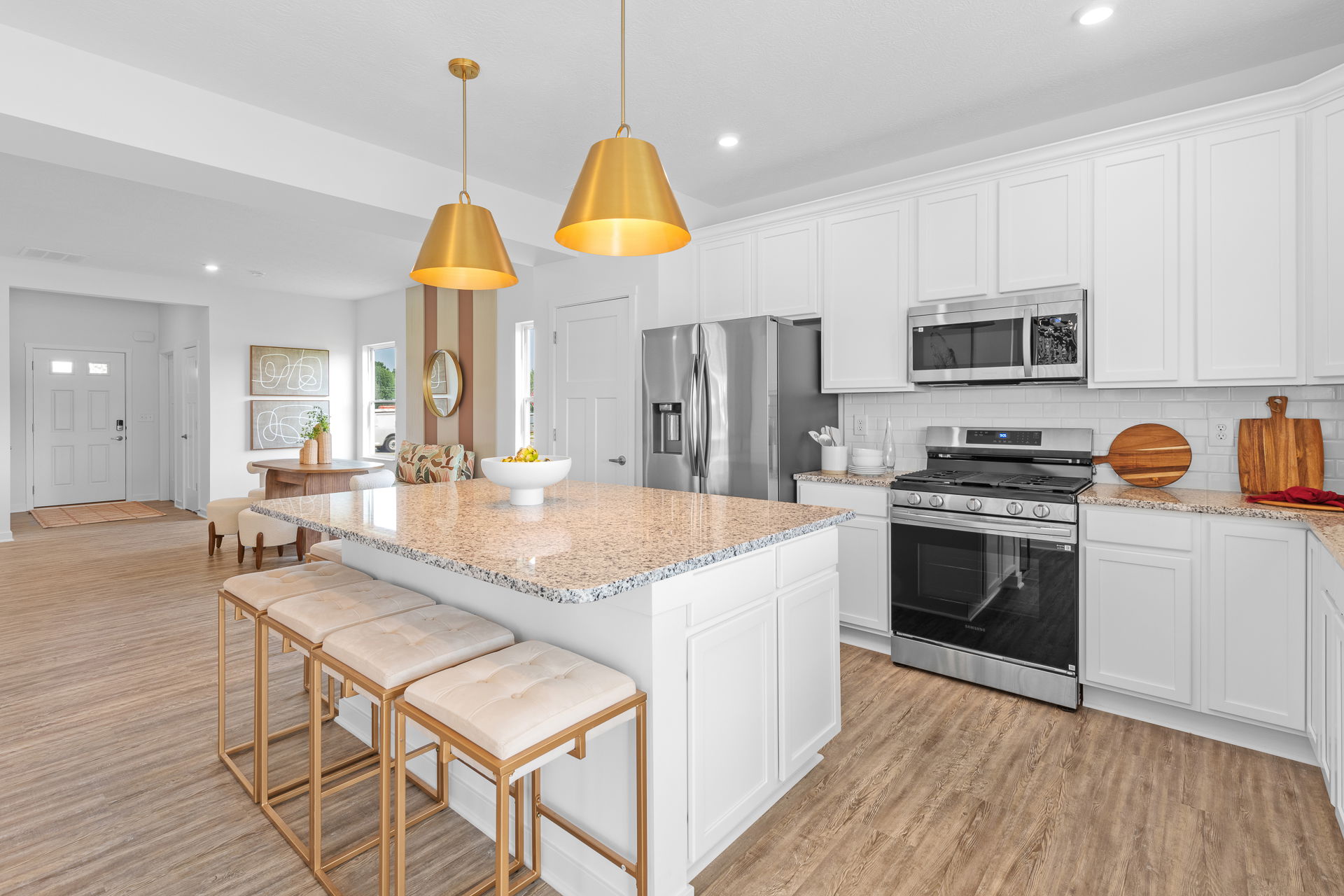 Modern kitchen interior featuring white cabinets, stainless steel appliances, a large center island with seating, and stylish gold pendant lighting.