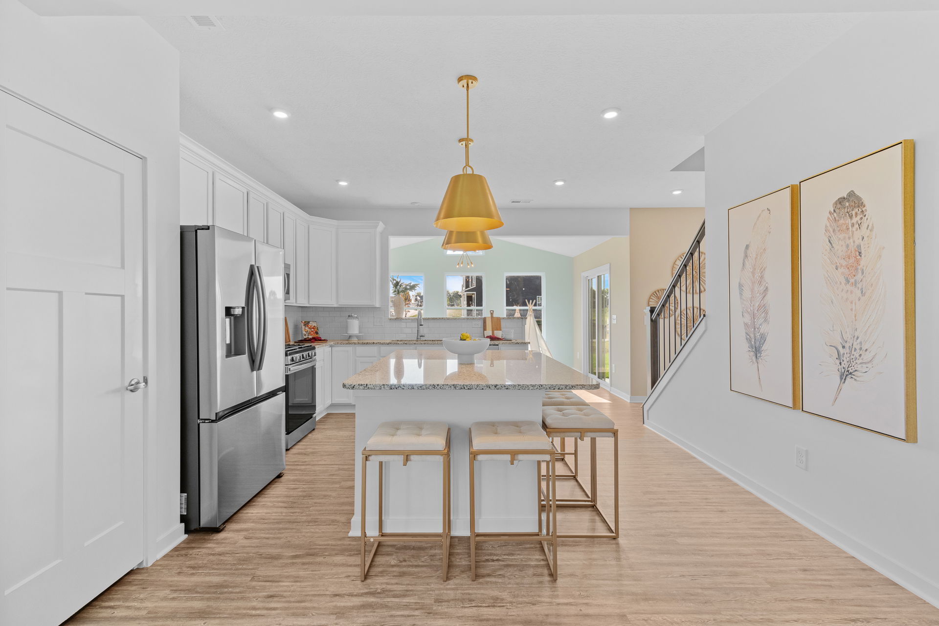Modern white kitchen with stainless steel appliances, granite island, and gold pendant lighting.