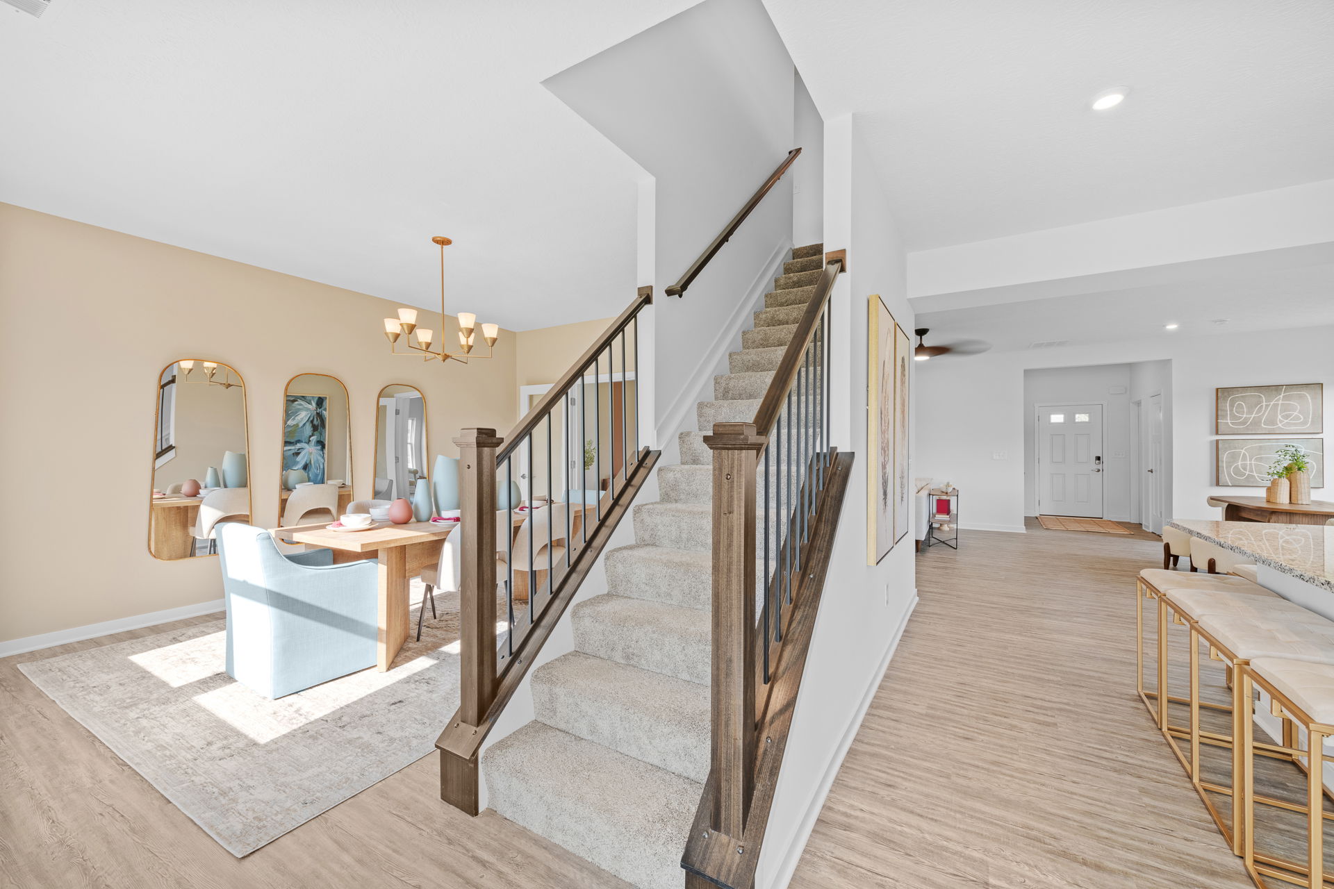 Modern open-concept home interior featuring a wooden staircase, dining area with elegant mirrors and chandelier, and light wood flooring.