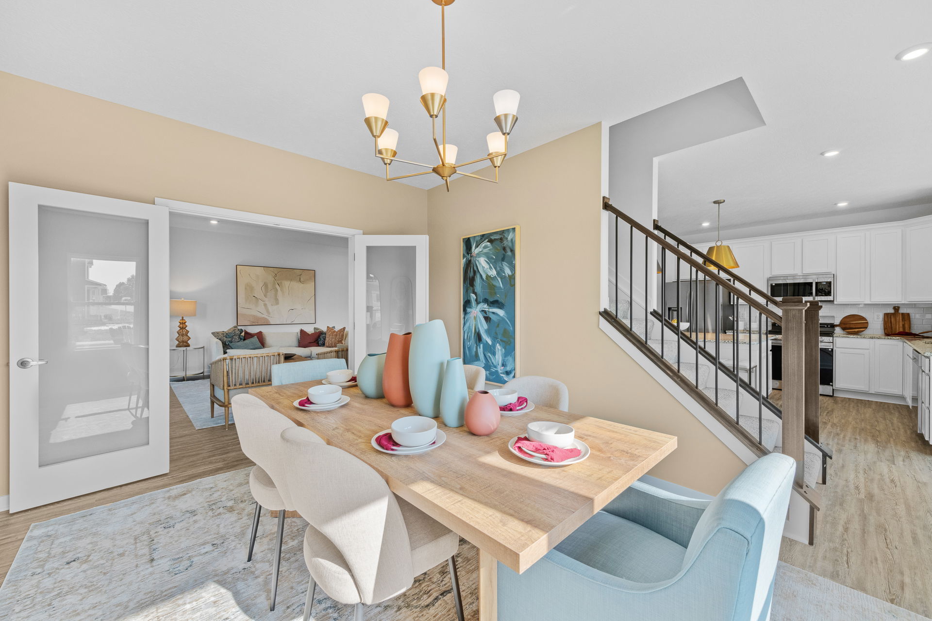 Modern dining room with wooden table, pastel vases, and white kitchen in open-concept home.