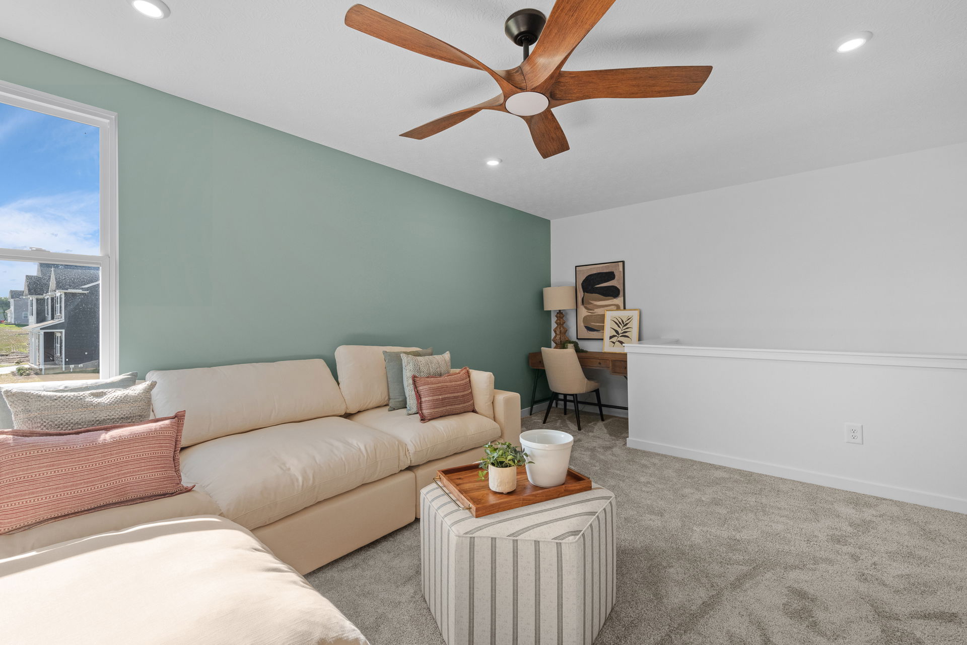 Bright and modern living room with beige sectional sofa, decorative pillows, mint green accent wall, and a stylish ceiling fan.