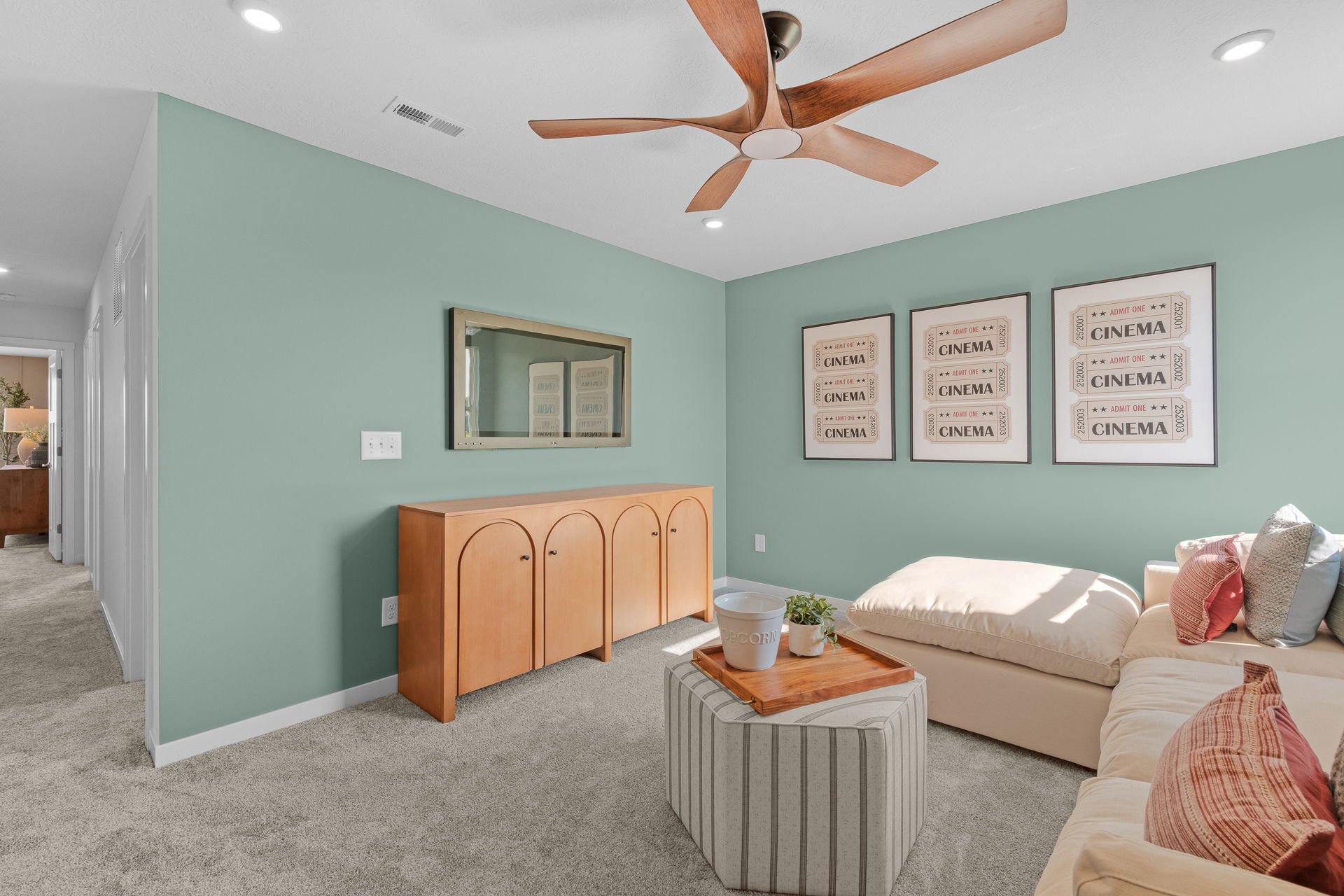 Stylish living room with green walls, wooden ceiling fan, cozy beige furniture, and cinema-themed wall art.