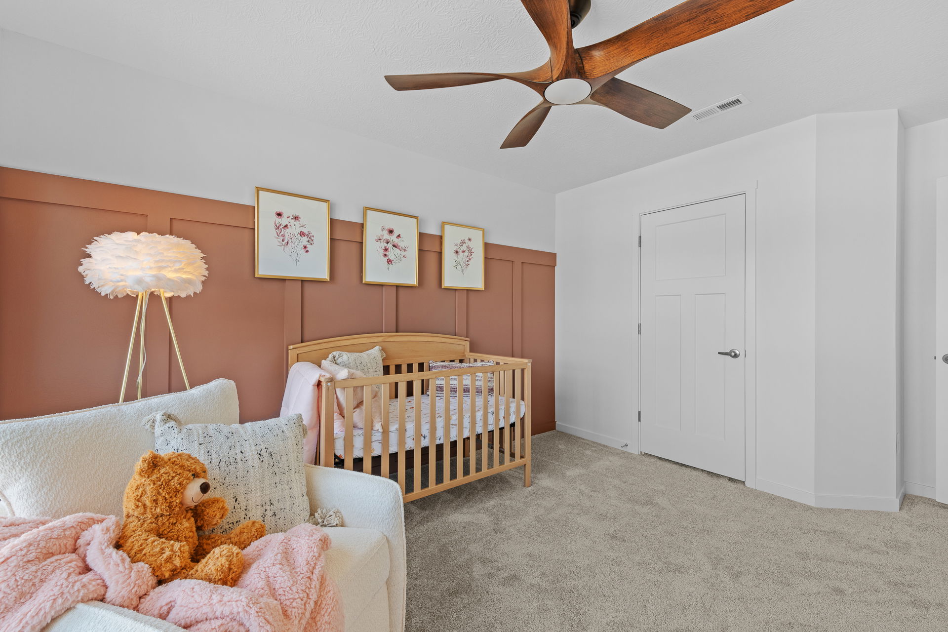 Modern nursery room with a wooden crib, cozy armchair, and pink accents, featuring a unique floor lamp and decorative floral wall art.