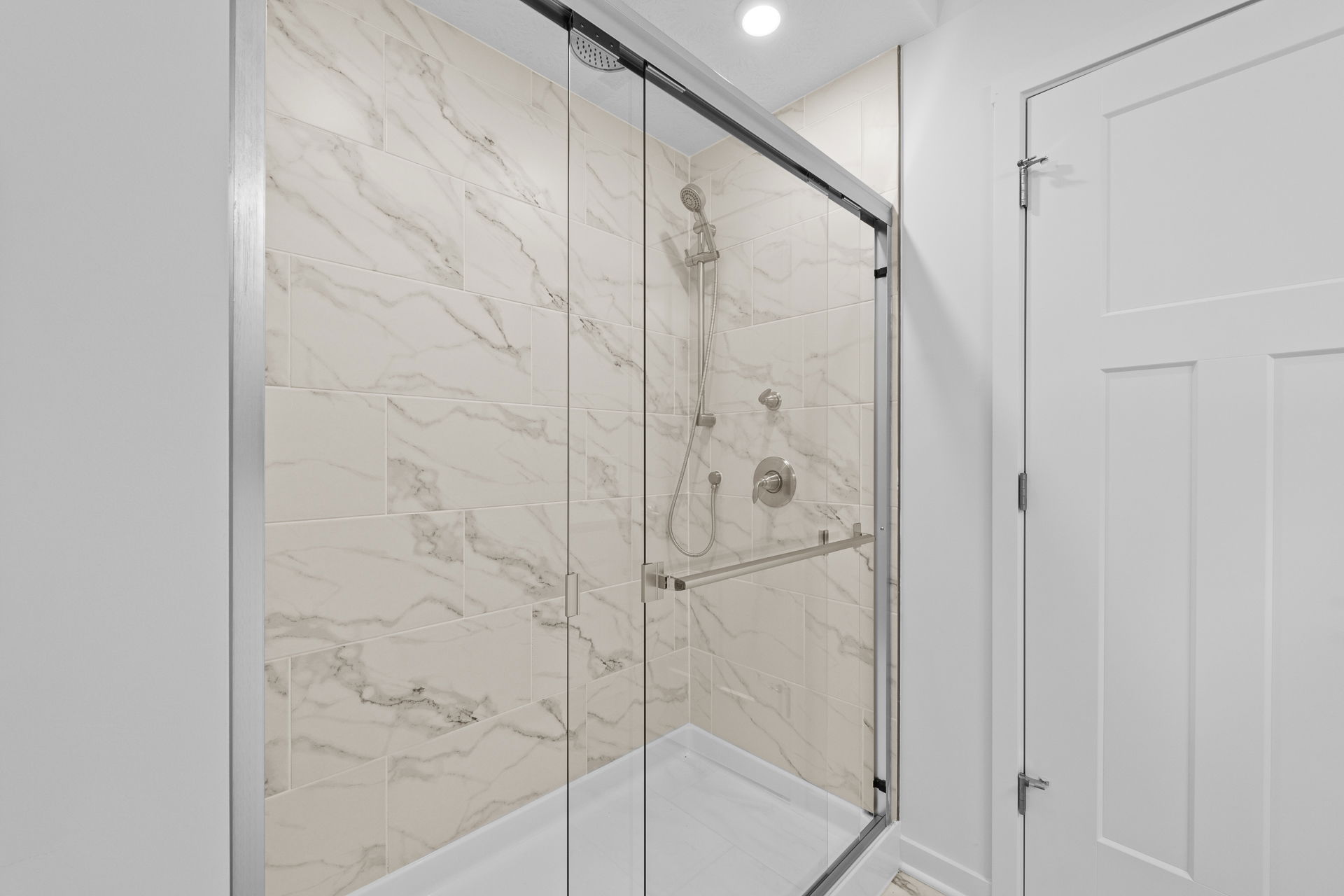 Modern bathroom with a glass-enclosed shower featuring beige marble-patterned tiles and stainless steel fixtures.