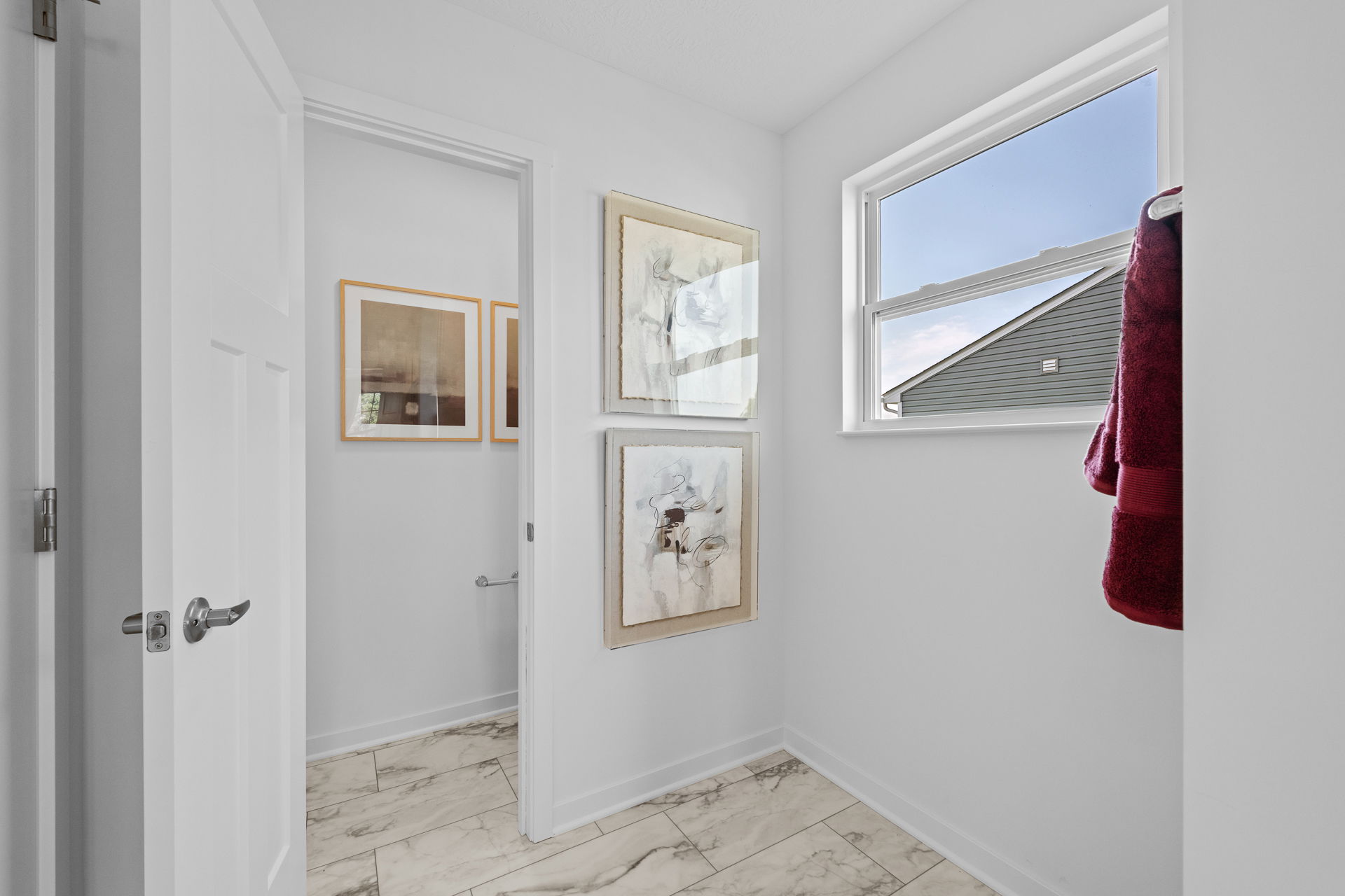 Modern white hallway with marble floor, abstract wall art, and a window view with red towels hanging.