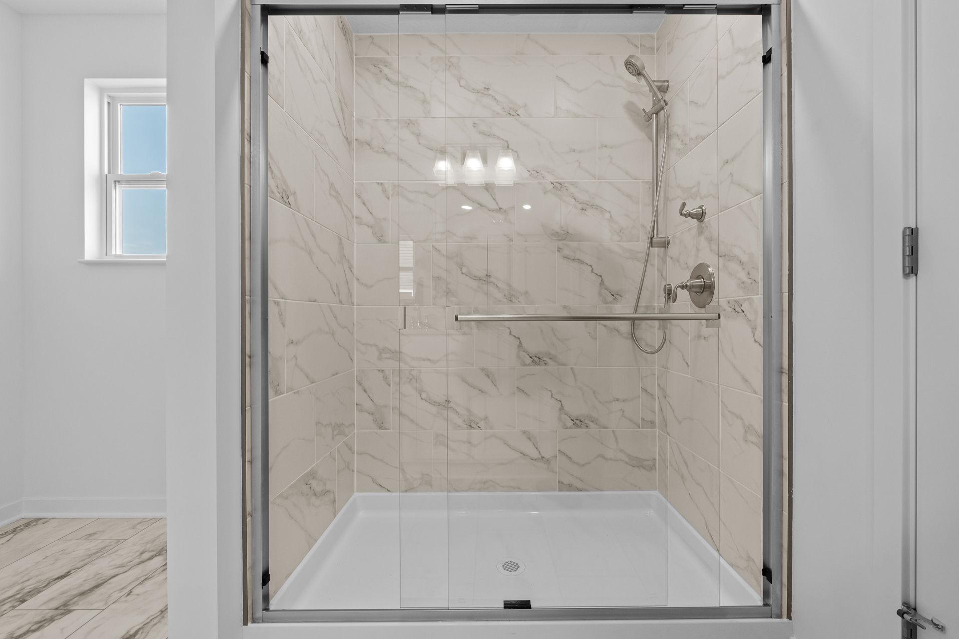 Modern bathroom with glass-enclosed shower featuring elegant marble-patterned tiles and chrome fixtures.