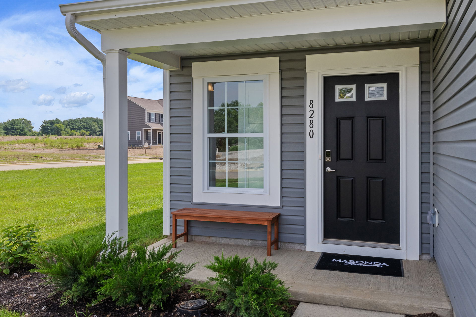 Front porch of a modern gray house with a black door, bench, and well-maintained lawn.