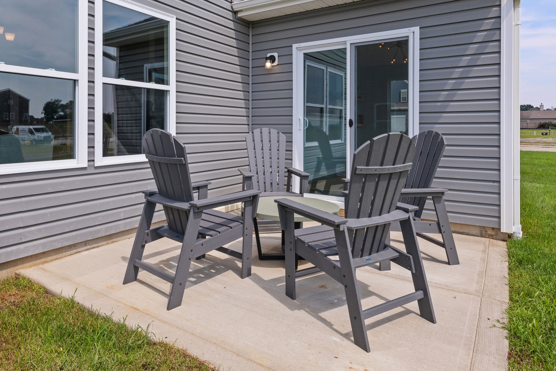Outdoor patio with four gray Adirondack chairs around a circular table next to a modern house.