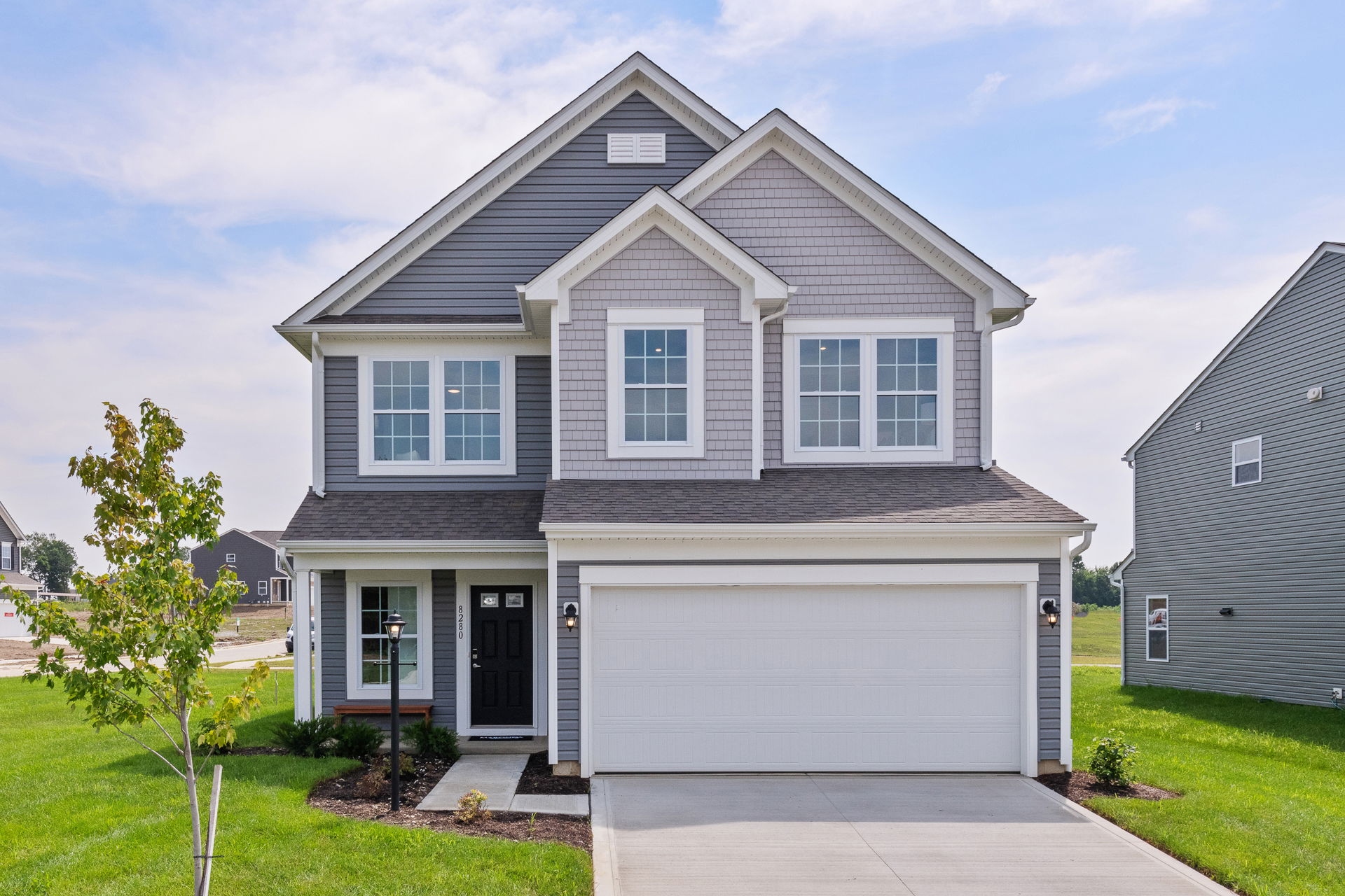 Modern, two-story suburban house with gray siding, white trim, and a two-car garage, set on a neatly landscaped yard.