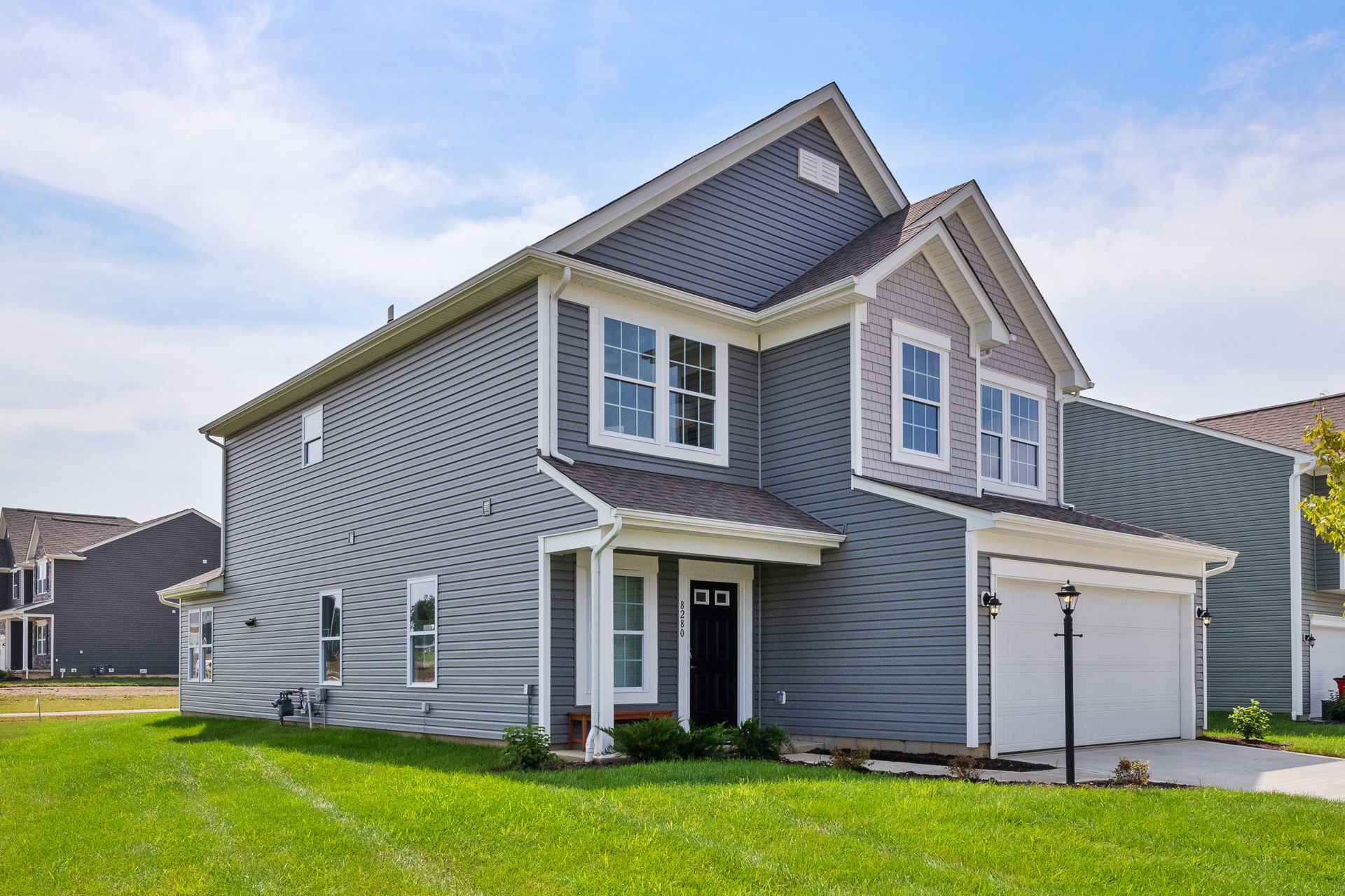 Modern two-story gray house with a garage and well-maintained green lawn under a clear sky.